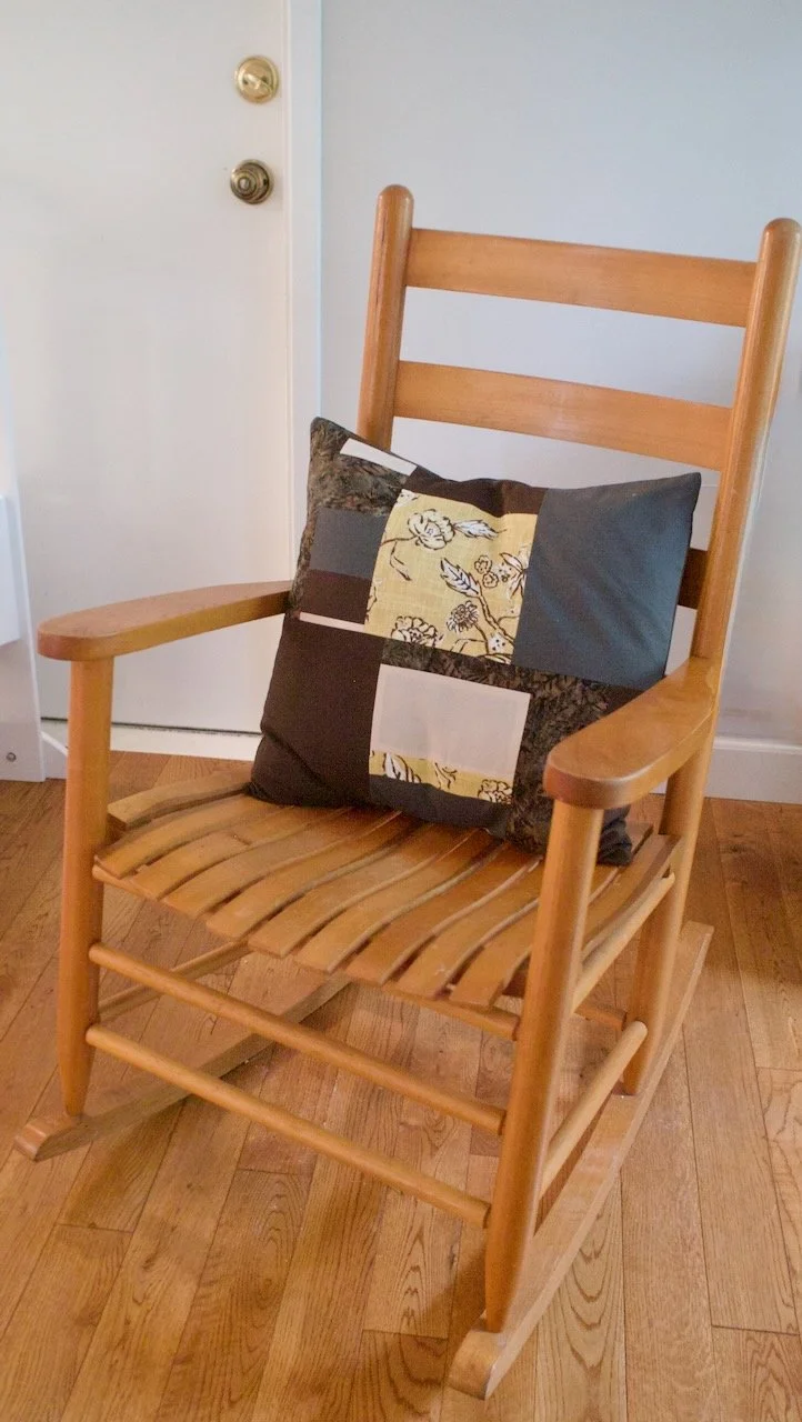 Wooden rocking chair with a patchwork pillow on the seat, placed on a hardwood floor near a white door.
