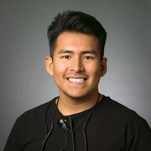 Dr. Saul Gonzalez, dark hair smiling, wearing a black shirt and a headset, against a gray background.