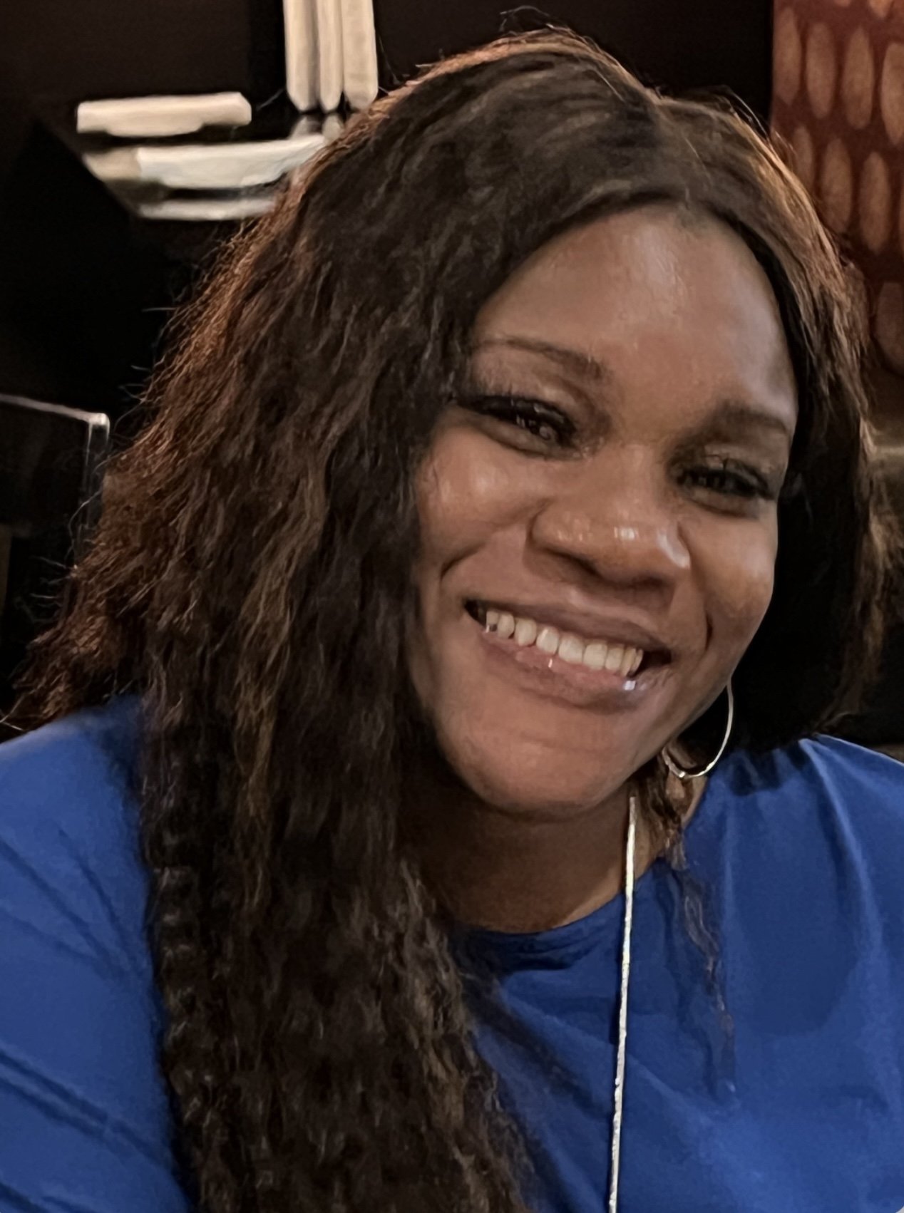portrait photo of a black woman with brown hair, a silver hoop earring, and wearing a deep blue blouse.