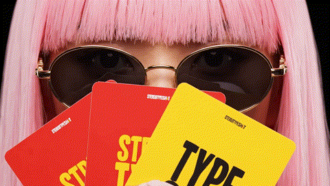 Person with long pink hair wearing black sunglasses, holding red and yellow cards with bold text.