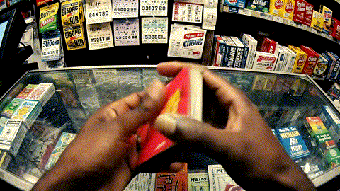 Person holding a red and yellow candy or snack at a convenience store checkout counter with various products and coupons in the background.