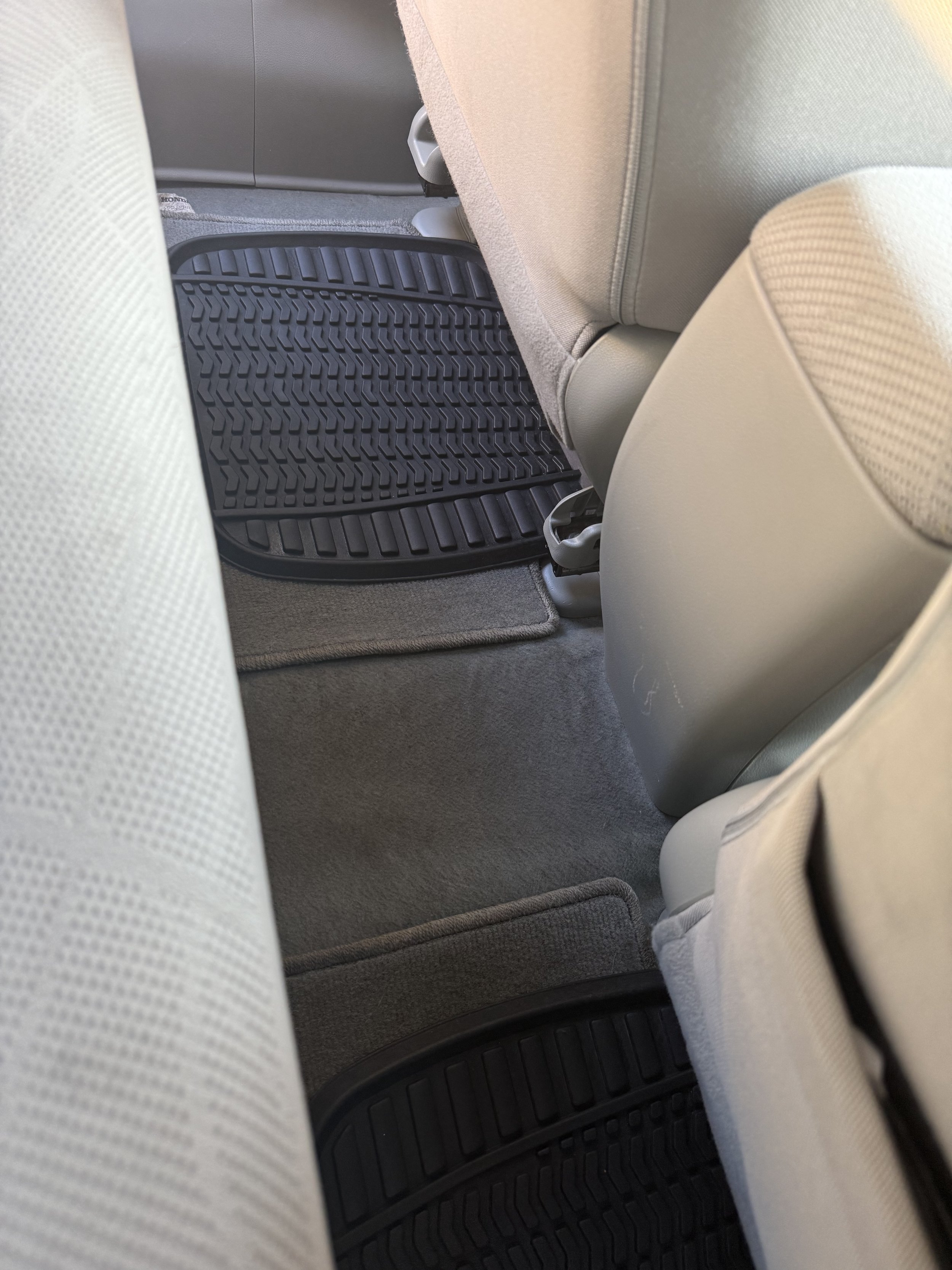 The backseat floor of a car with beige seats and black rubber floor mats.