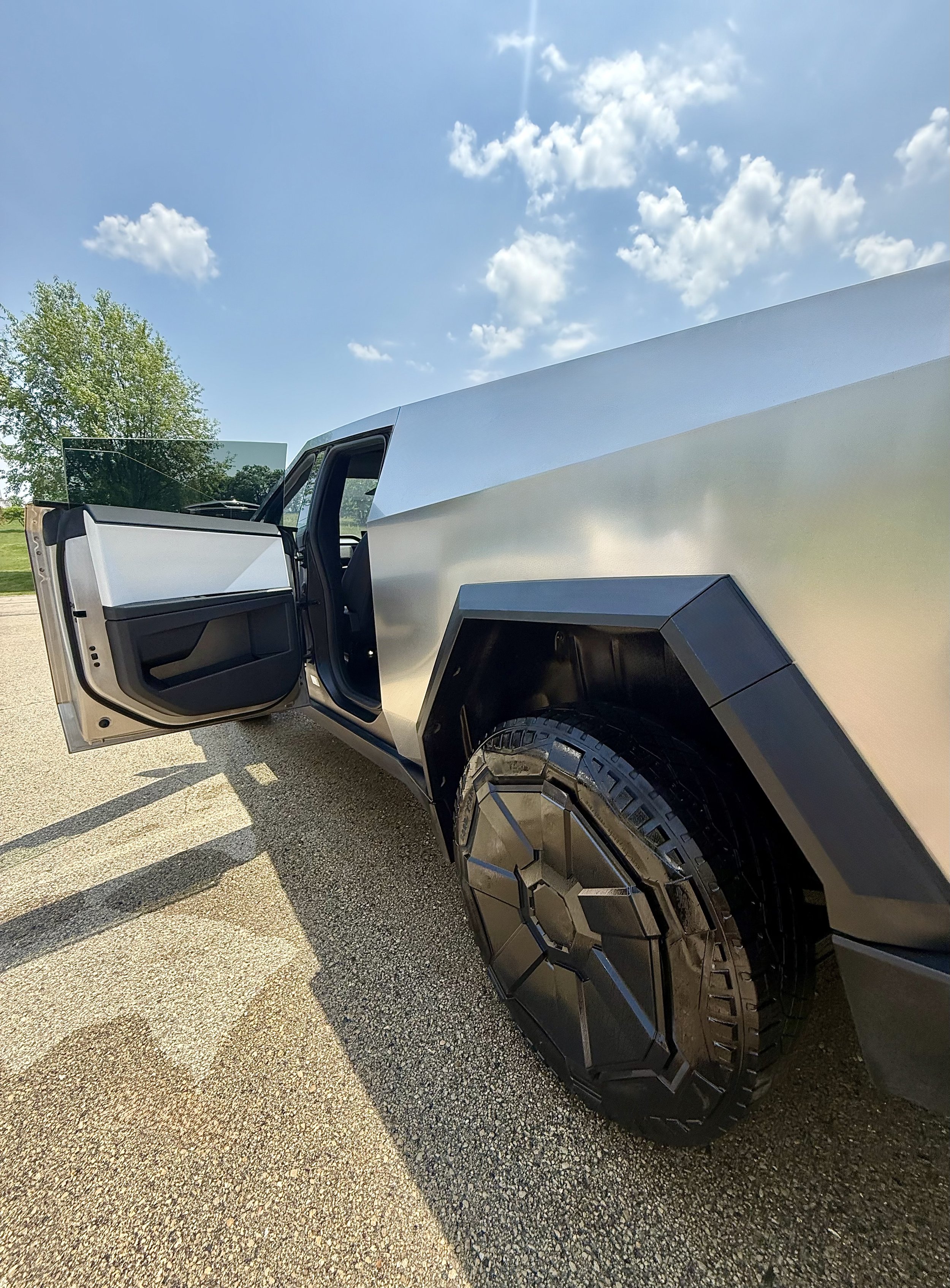 Front side of a modern, angular silver electric pickup truck with open front door on a sunny day.