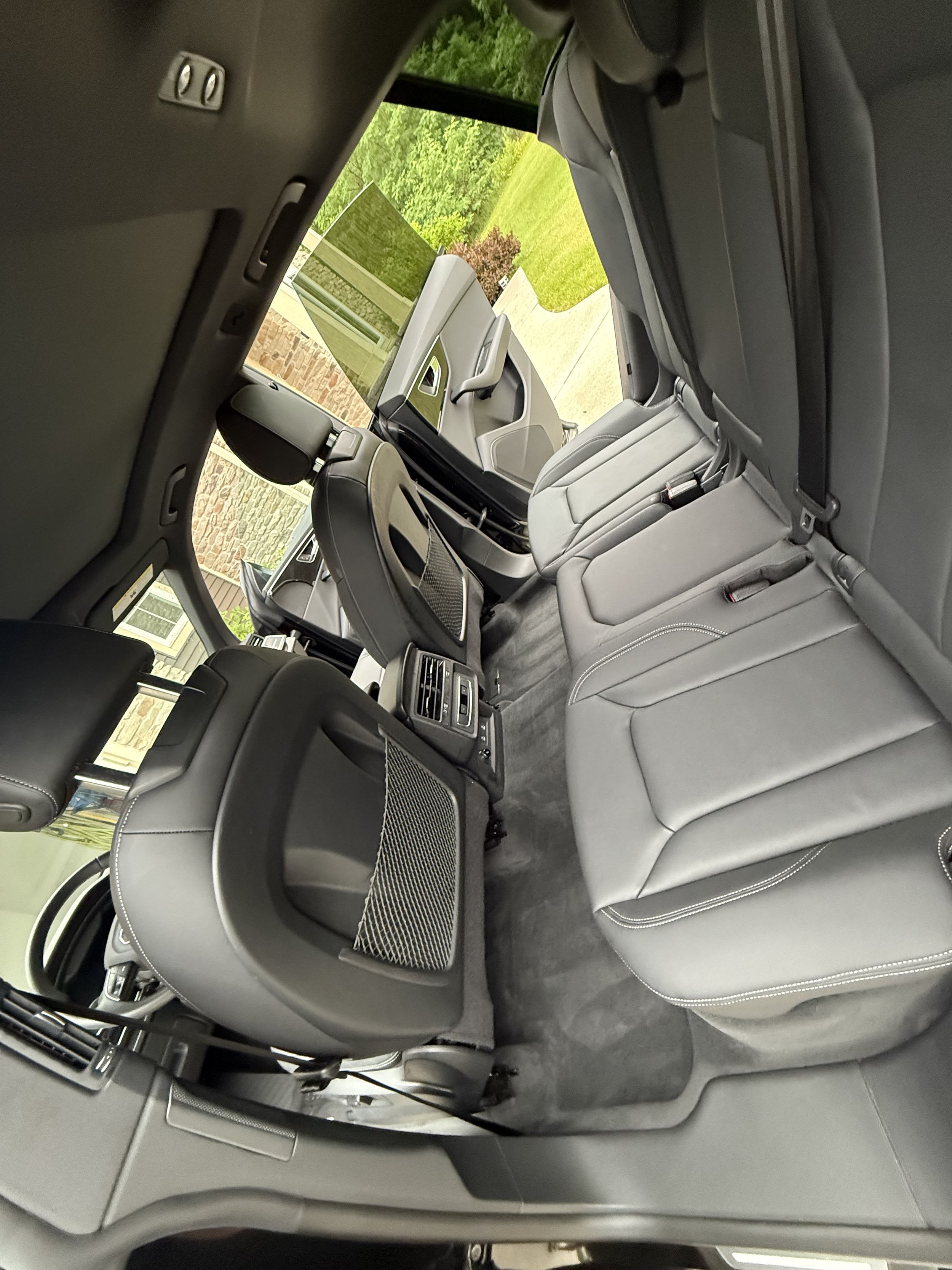 Interior view of a modern SUV showing the back seats, front seats, and dashboard with a view through the driver's side window of a green grassy yard and sidewalk.