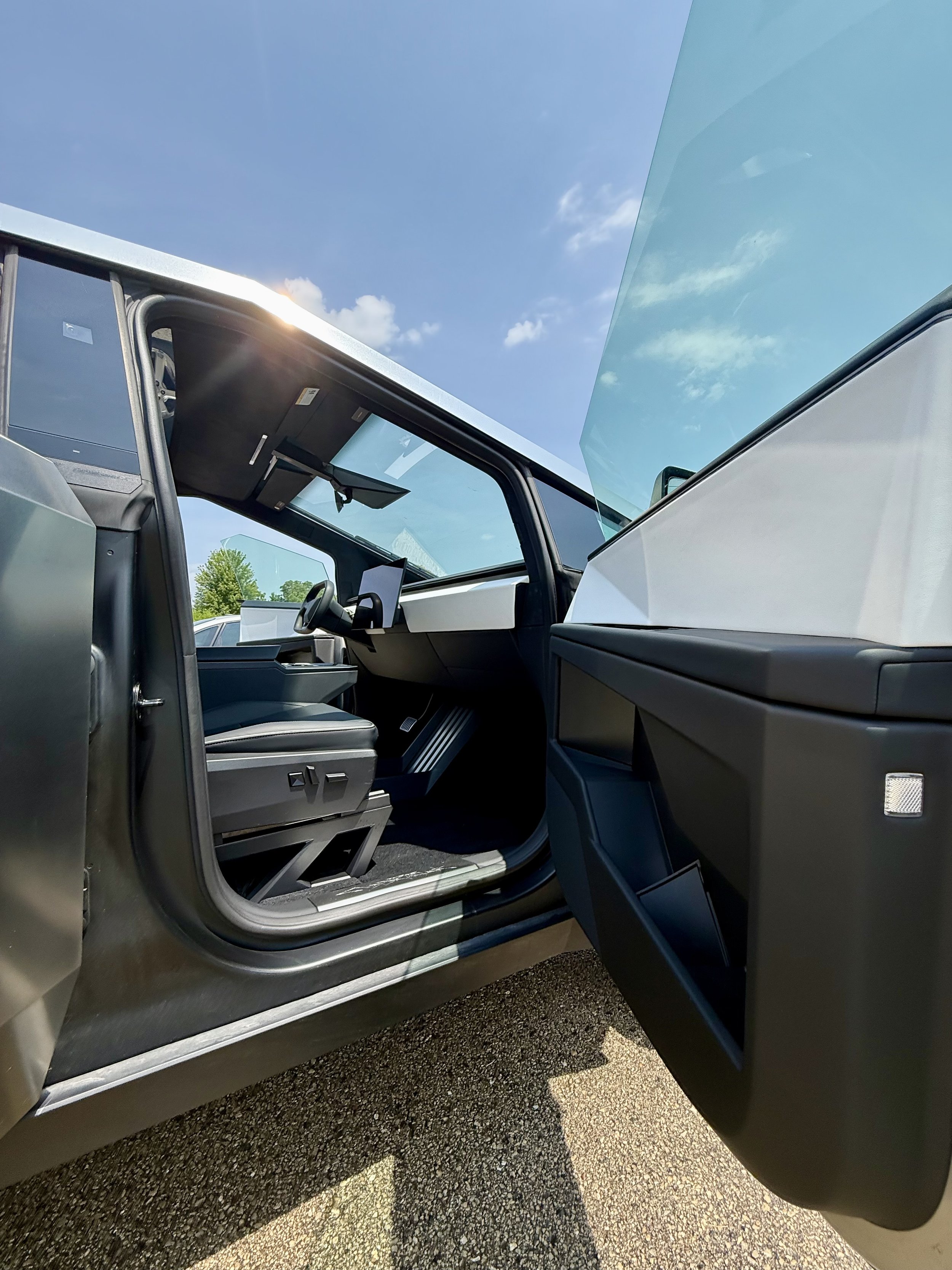 Open door of a futuristic electric vehicle showing interior with digital display, steering wheel, and modern design, under a blue sky with some clouds.