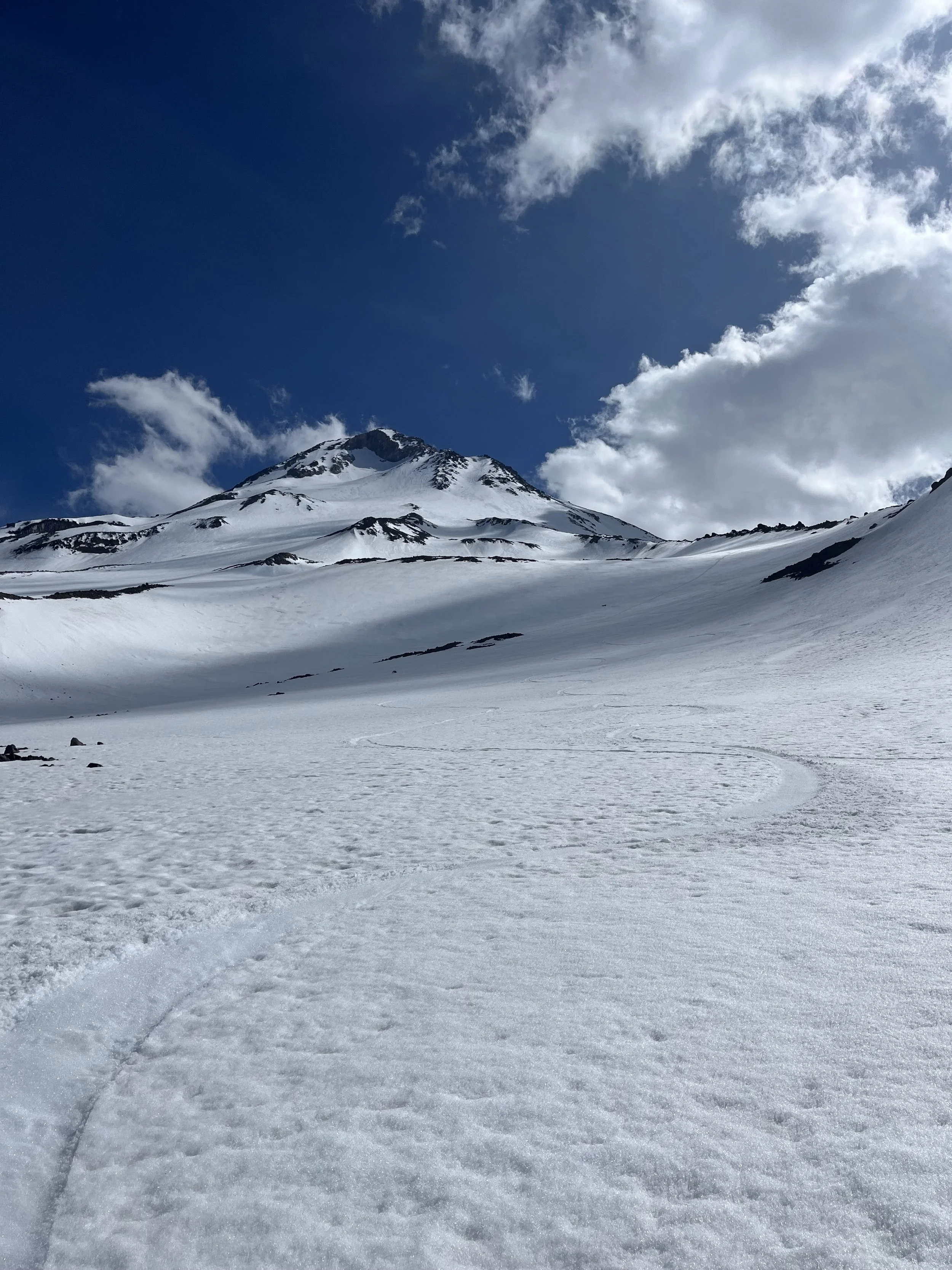 Snow-covered mountain landscape with a clear blue sky and scattered clouds.