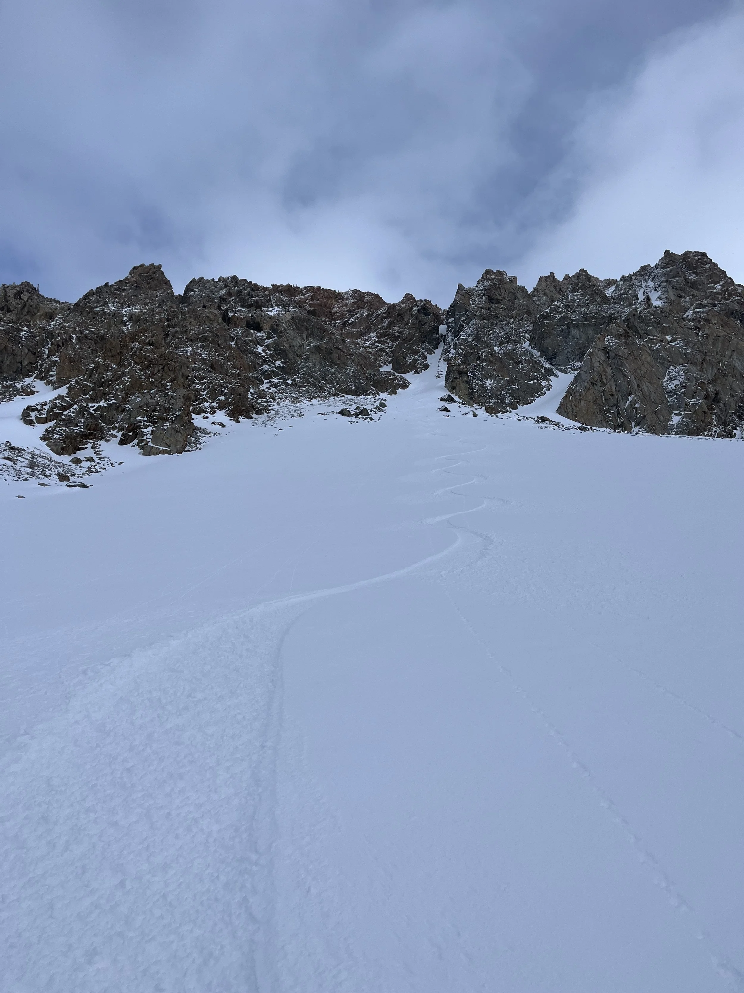 Snow-covered mountain slope with rocky peaks in the background and ski tracks in the snow.