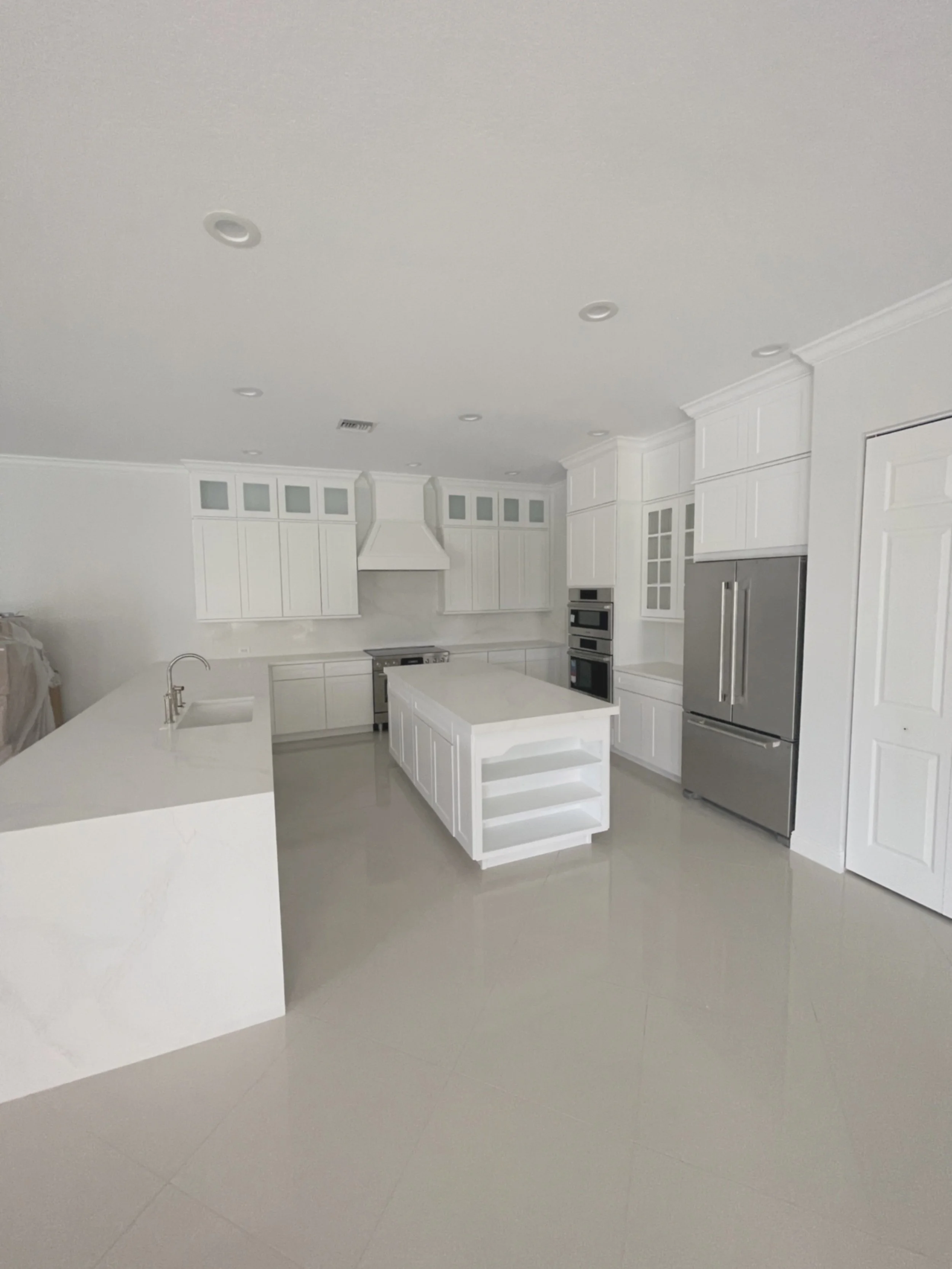 Empty modern white kitchen with stainless steel appliances, central island with open shelves, and white cabinetry.