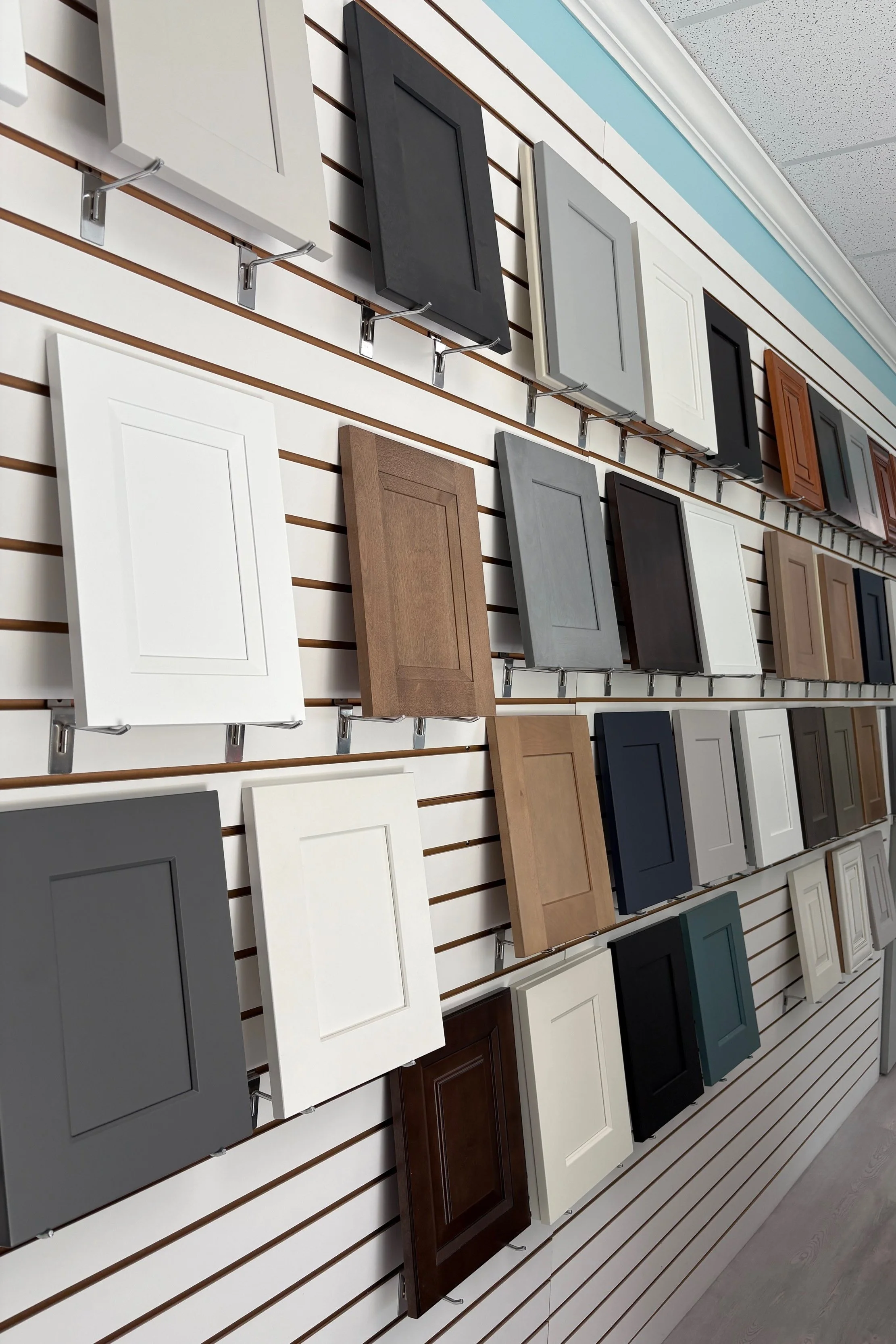Display of cabinet door samples in various colors and finishes on a slatwall at a retail store.