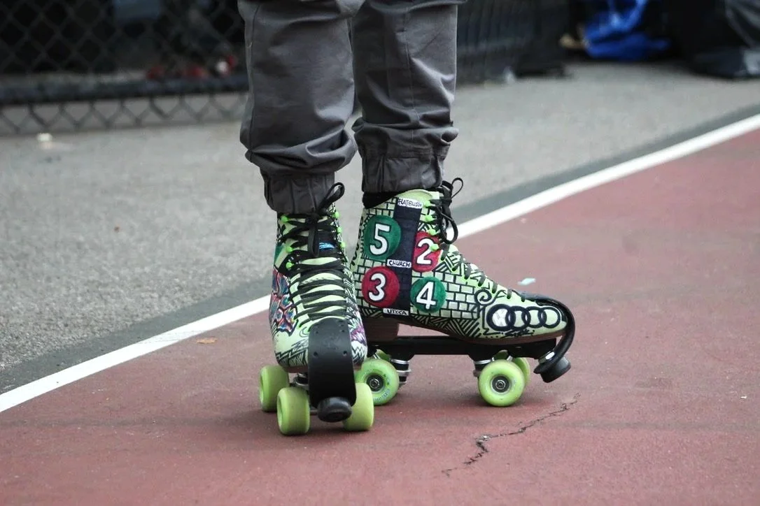 Close-up of a person wearing a colorful roller skate with cartoon and graffiti designs, standing on a red playground surface with a white line.