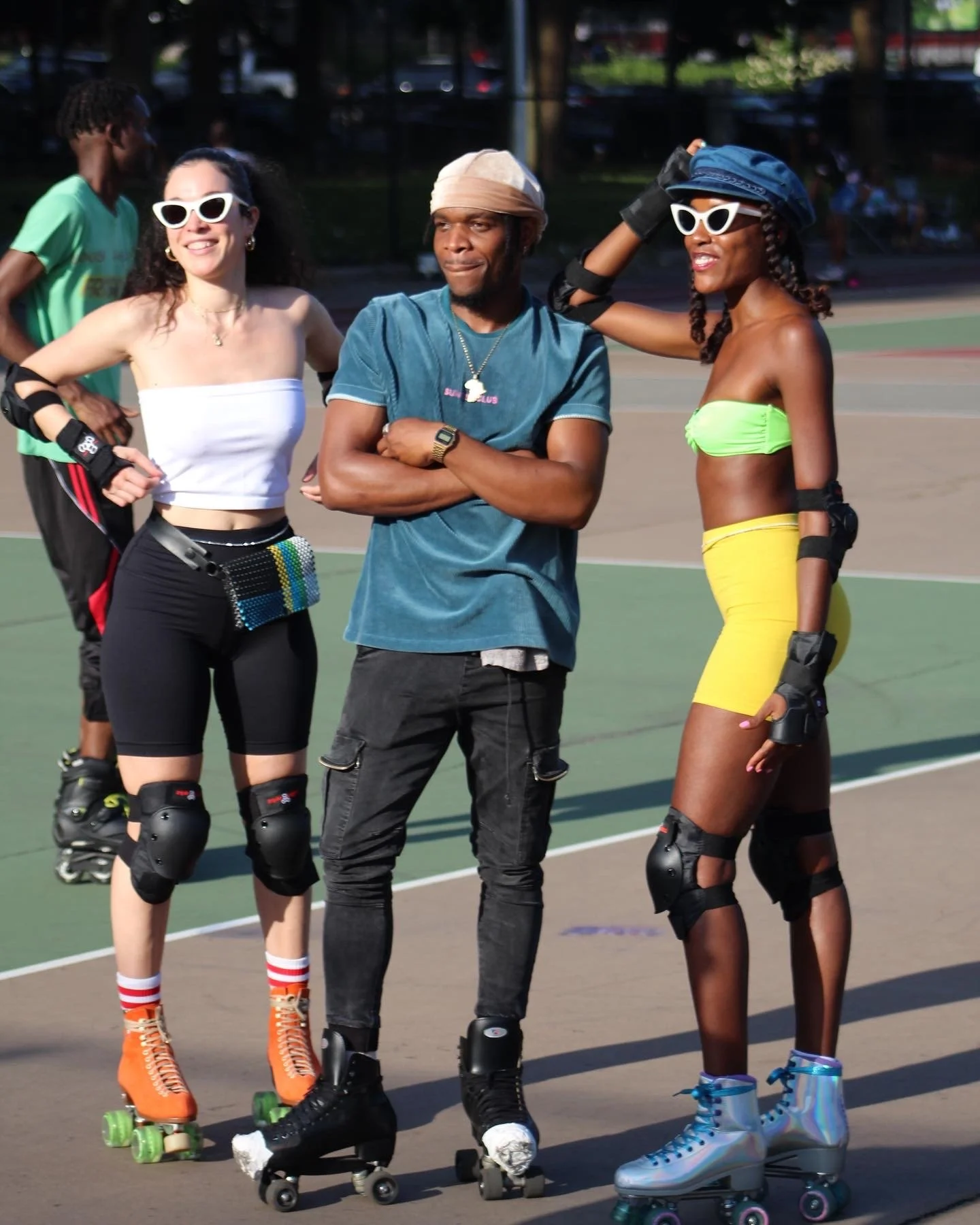 People in colorful outfits wearing roller skates on an outdoor court, with two women wearing sunglasses and a man in the center.