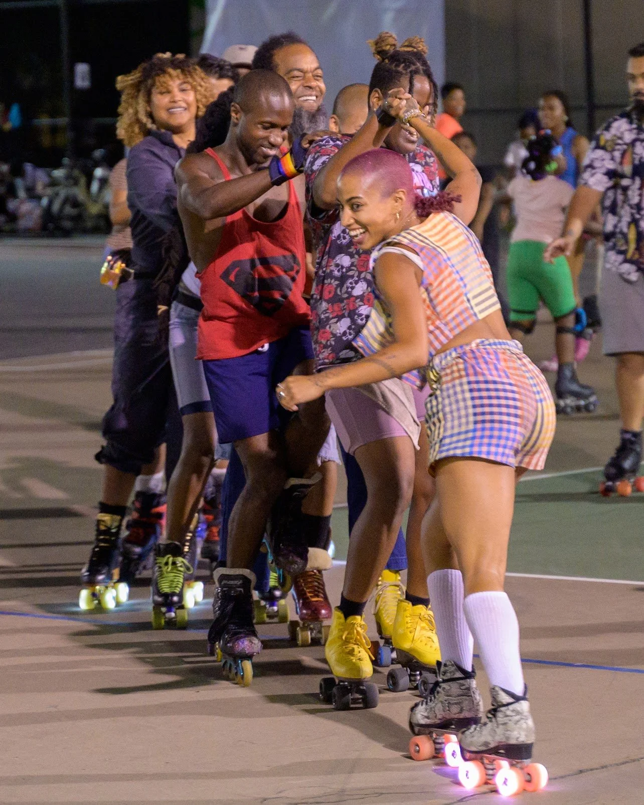 A group of people roller-skating together on an outdoor rink at night, smiling and enjoying themselves.