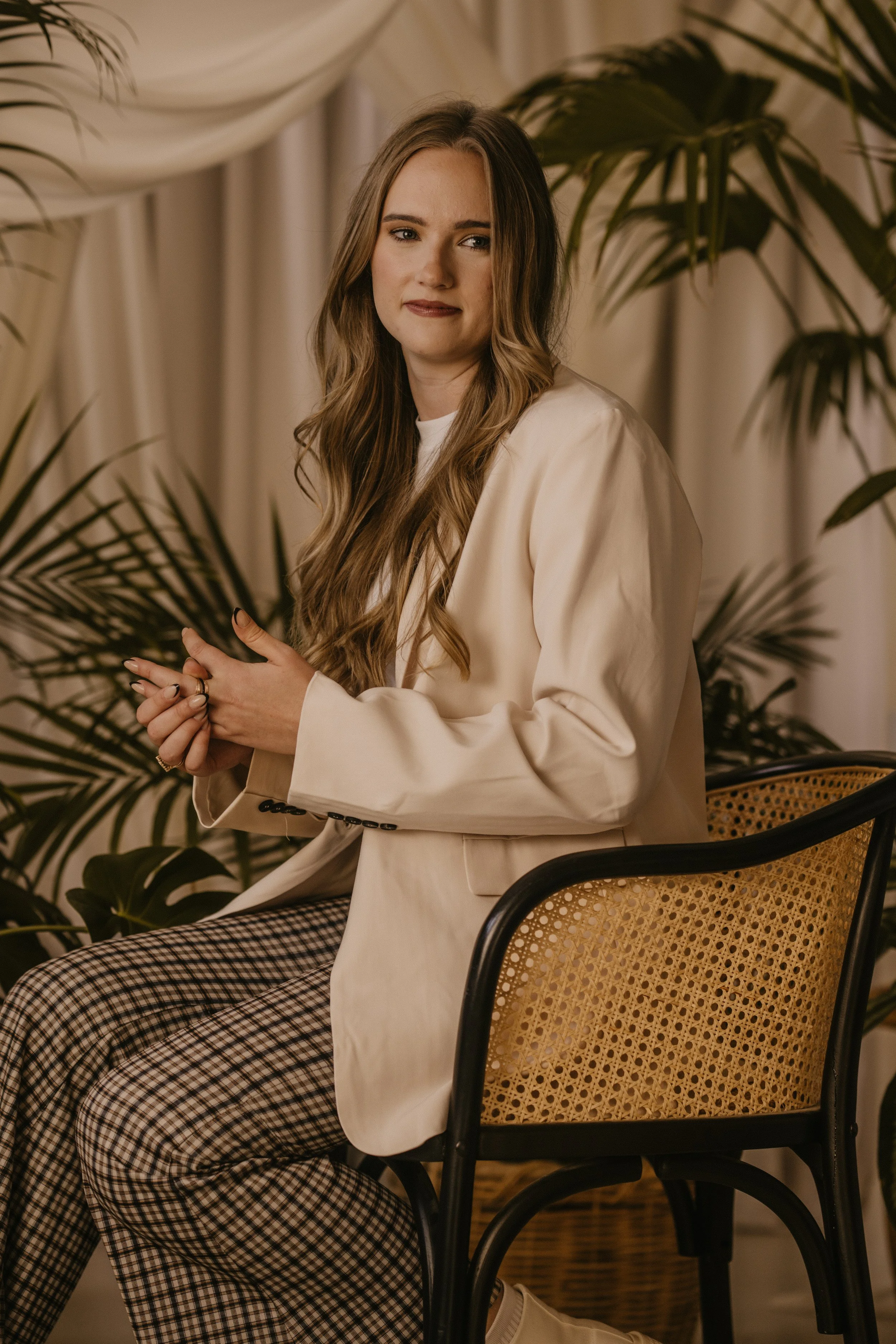 madeline sits posed in a chair thinking and staring off past the camera green plants and professional clothes
