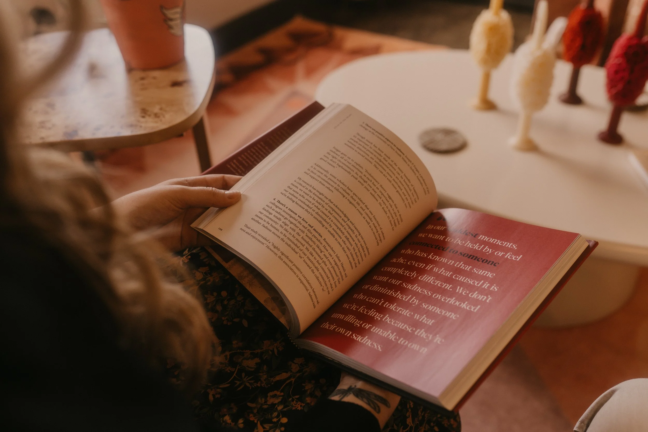 madeline is sitting on couch in Casa Hogar office holding a book by brené brown called the atlas of the heart