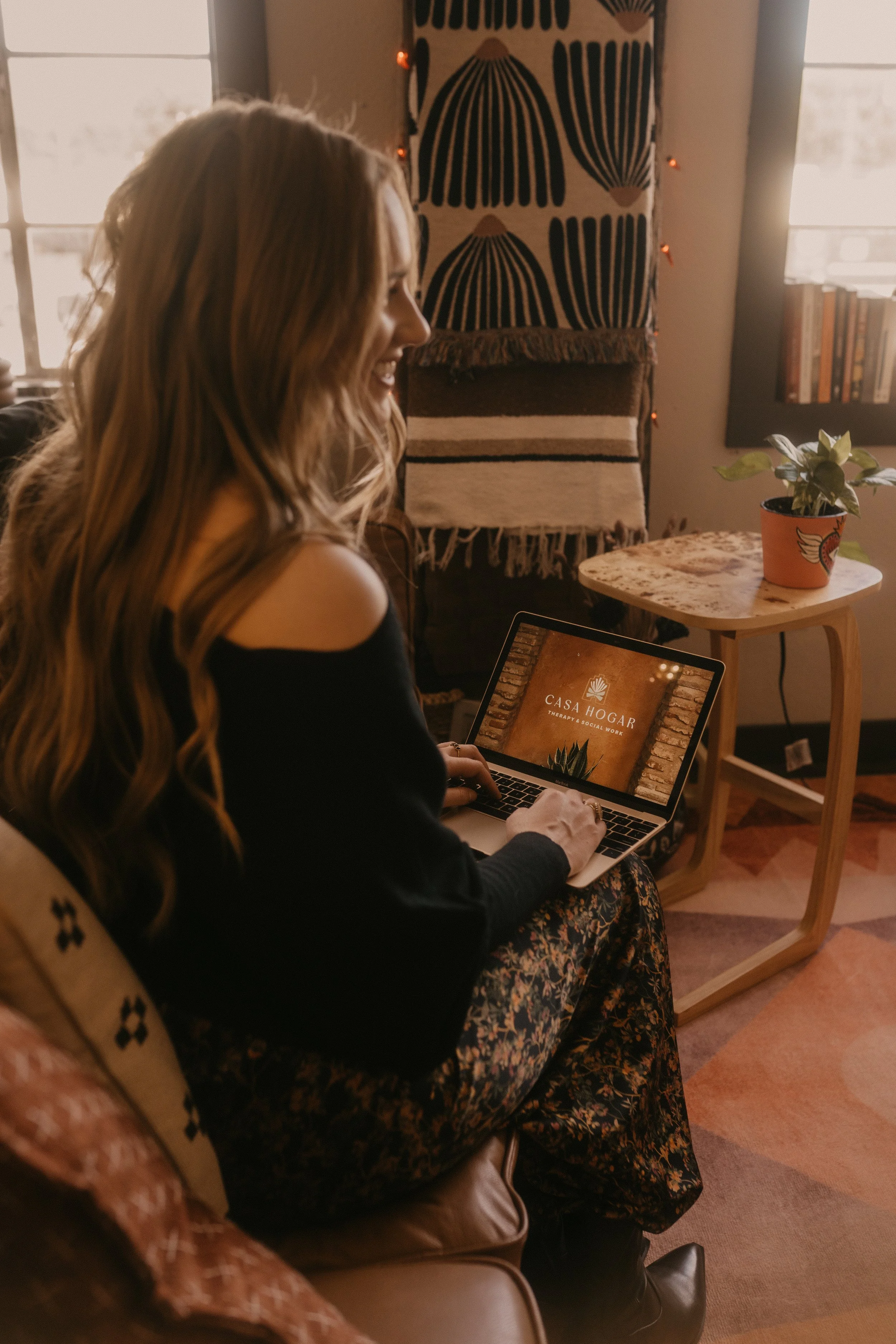 Madeline working on computer laptop smiling talking to client Casa Hogar office