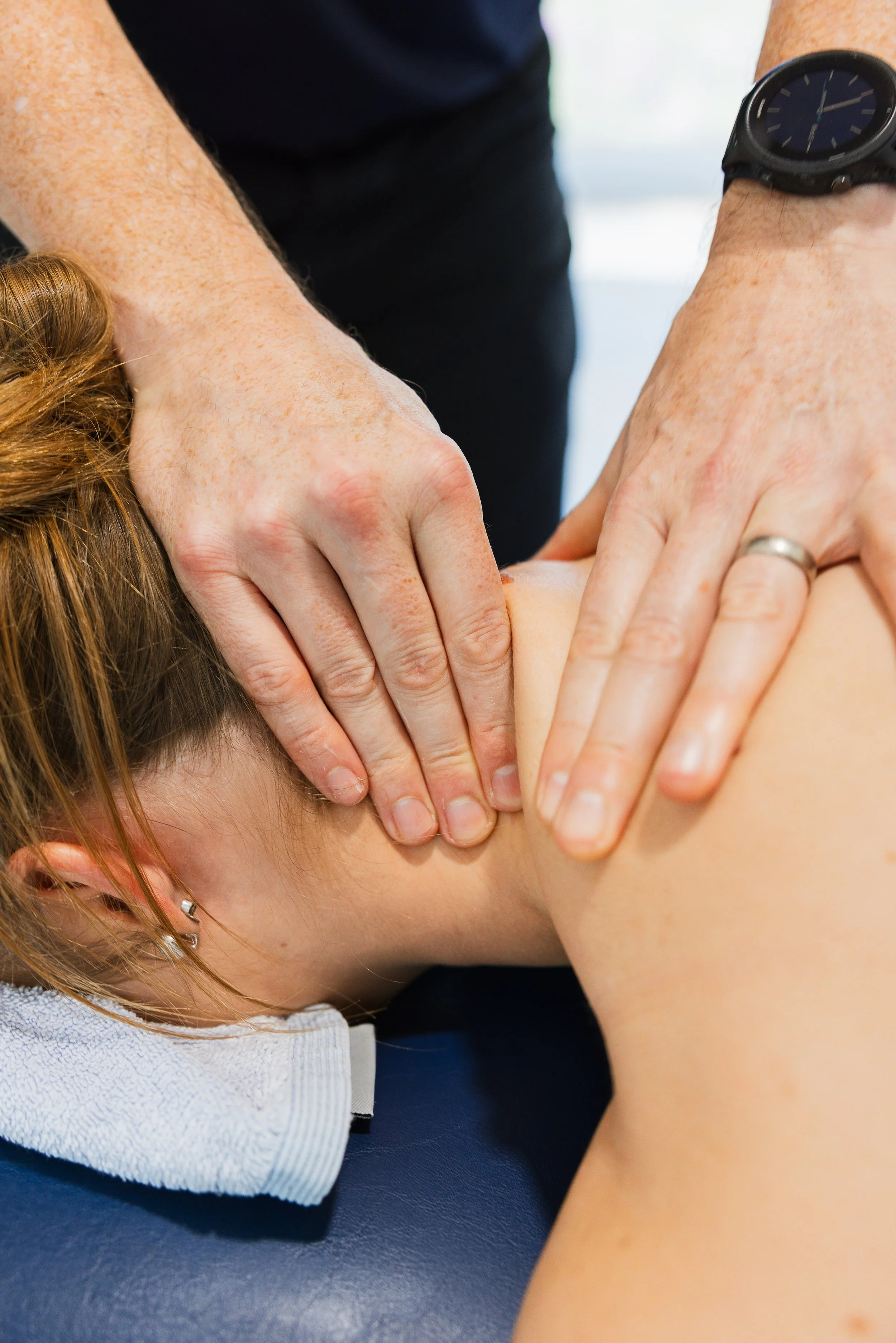 A person receiving a massage on their neck with massage therapist's hands applying pressure.