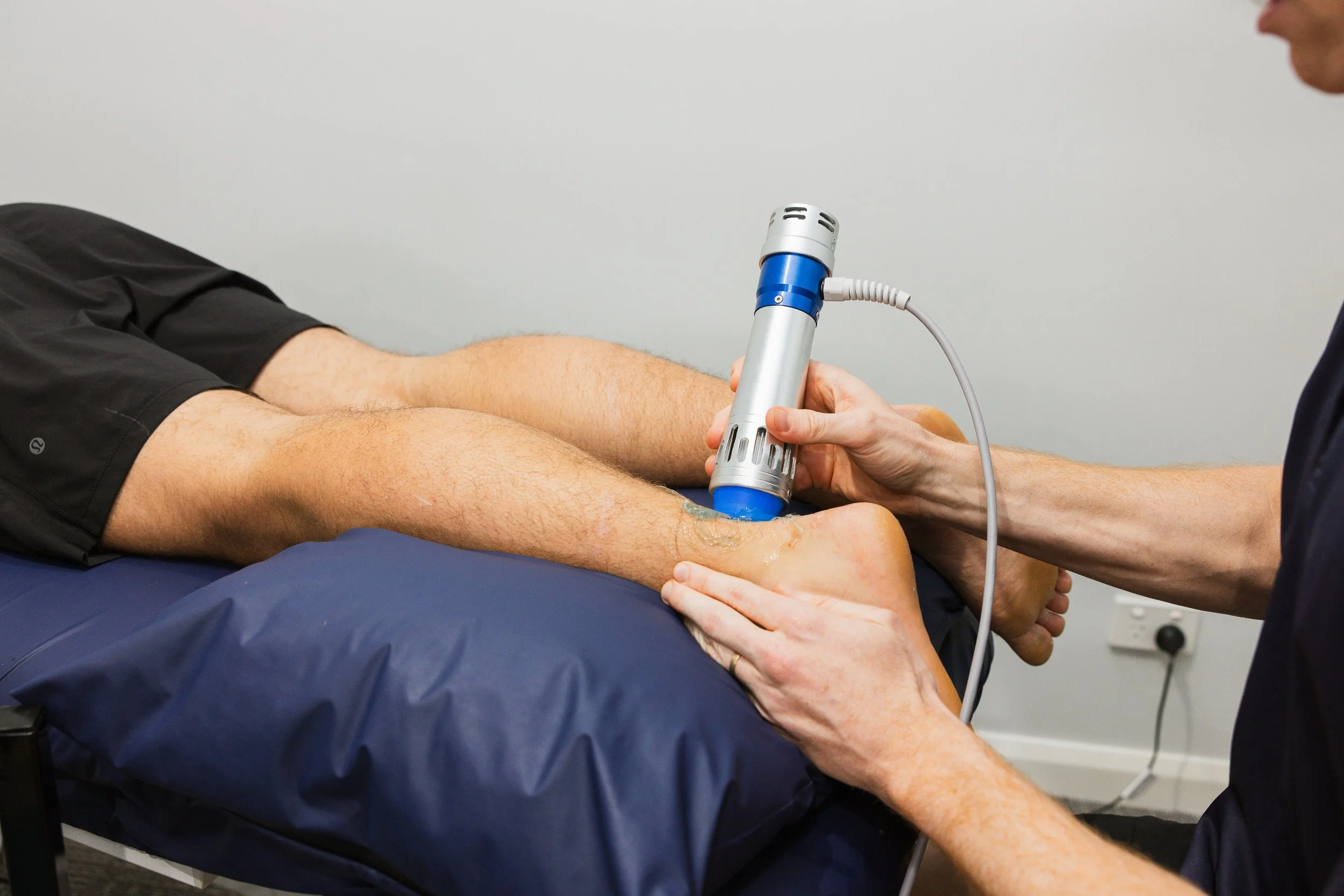 Medical professional applying shockwave therapy to a patient's lower leg and heel.