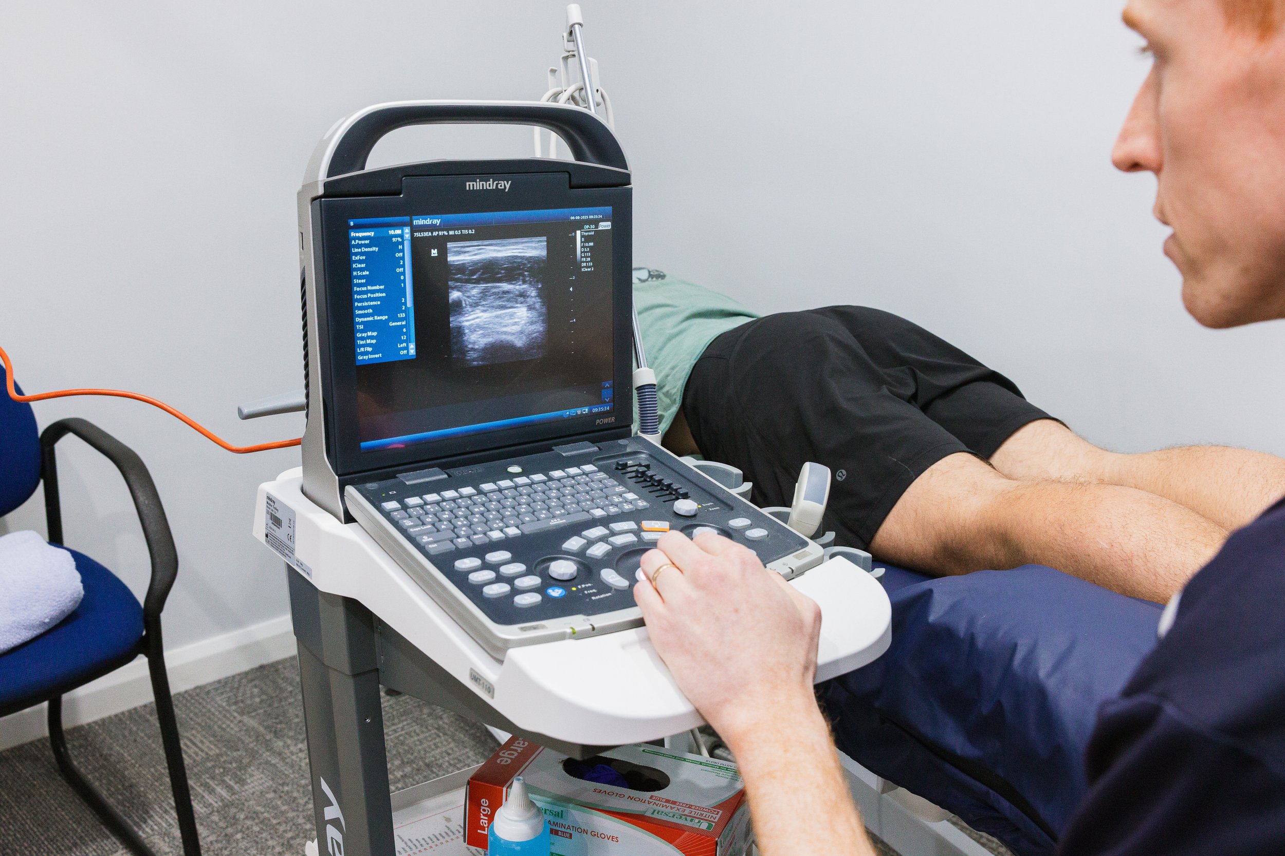 A healthcare professional conducting an ultrasound scan on a patient's abdomen in a medical office, with the ultrasound machine screen showing the image.