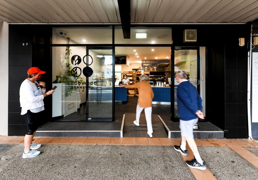 Bakery shop front with Goodwood Bakeshop sign on the window and two people entering the shop. One person waiting outside.