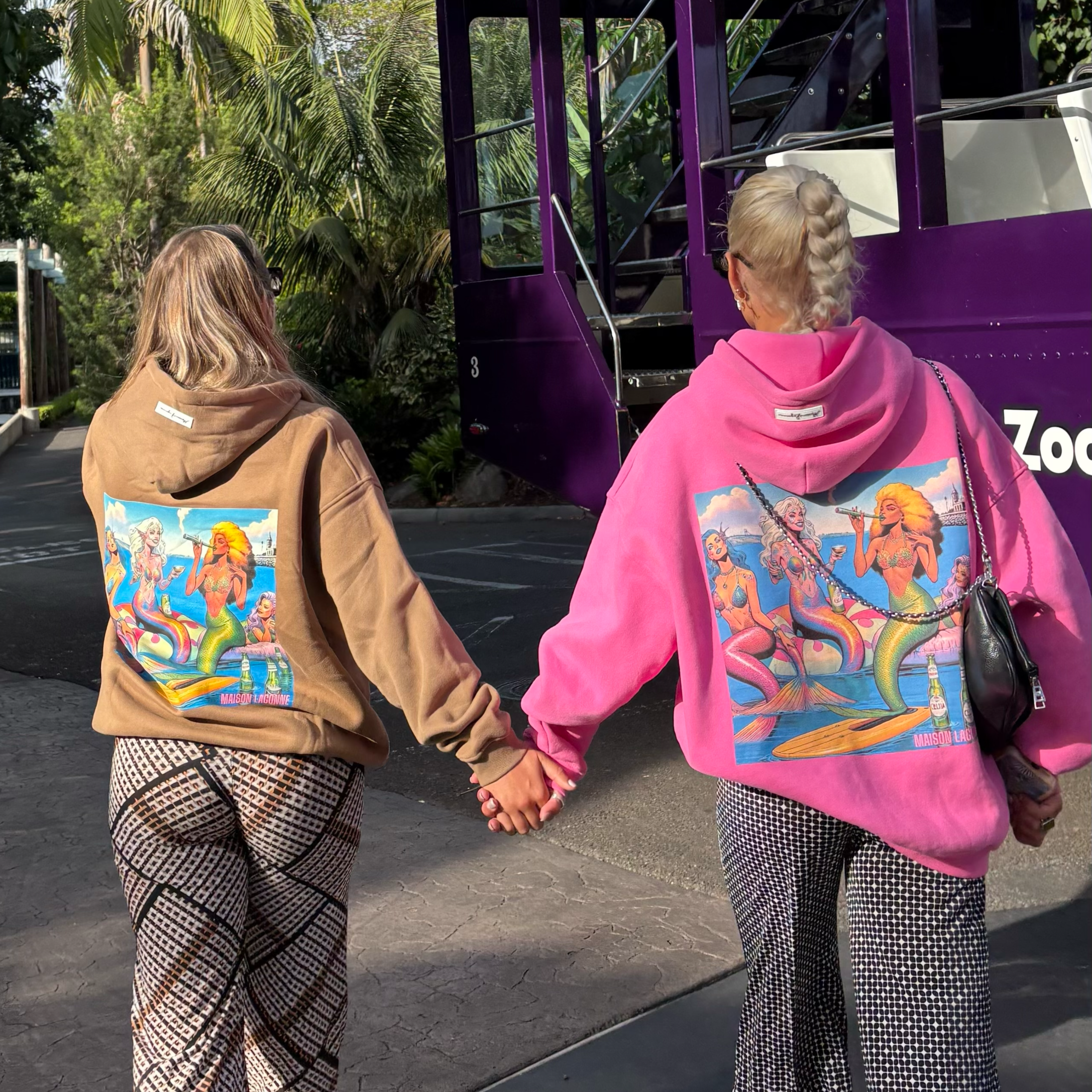 Two people wearing graphic mermaid hoodies in caramel and pink walking side by side.