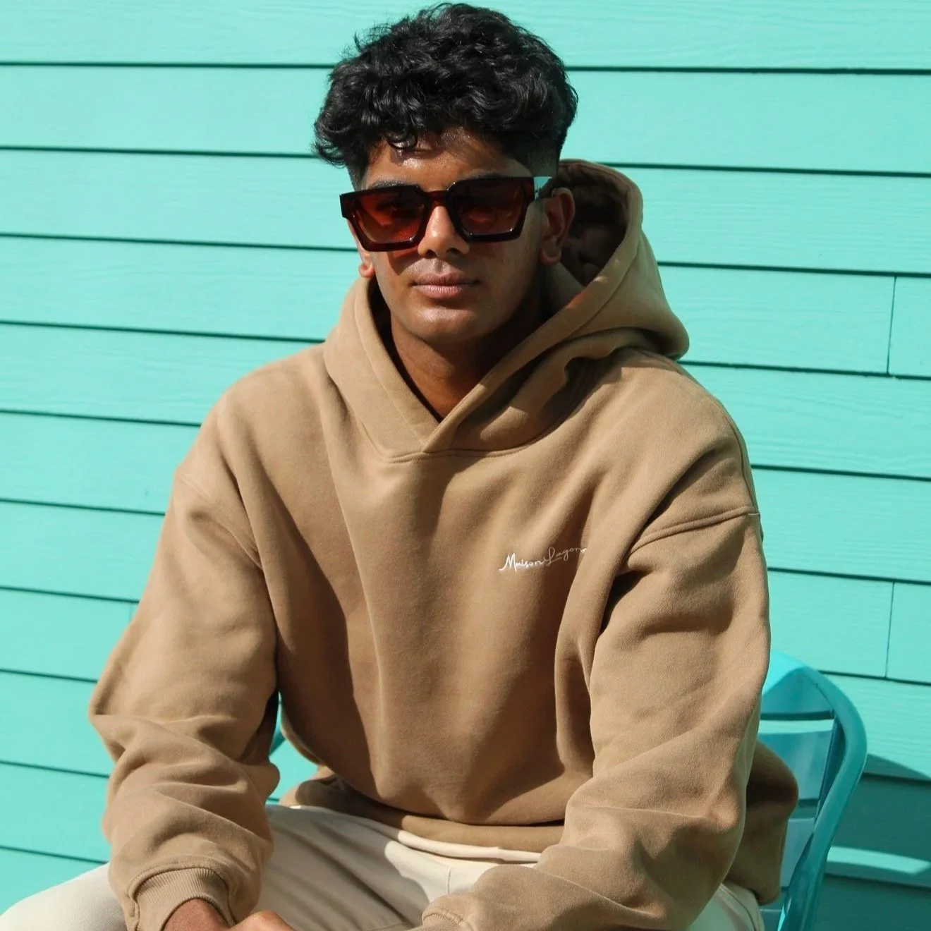 Caramel brown hoodie styled in a relaxed fit against a colorful wall.