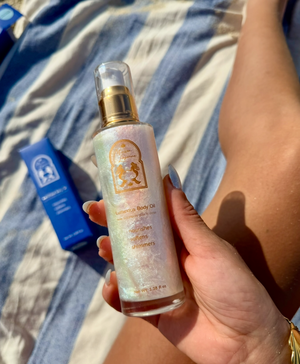 Luminous body oil bottle with shimmer finish held in natural sunlight.