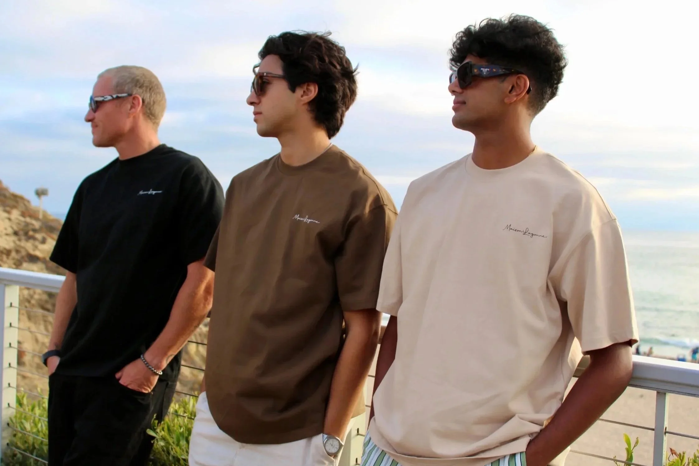 Three men wearing oversized t-shirts in neutral tones by the ocean.