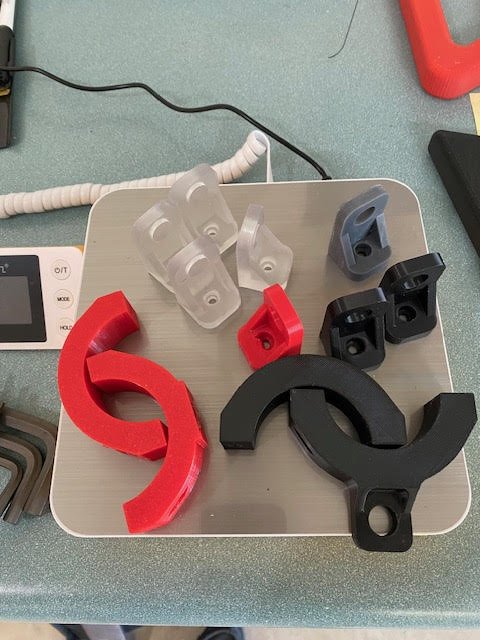 Various 3D-printed plastic clamp parts in red, black, gray, and white on a table.
