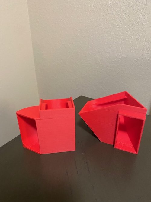 Red 3D-printed phone stands on a black surface against a white wall, with one stand upright and the other lying on its side.