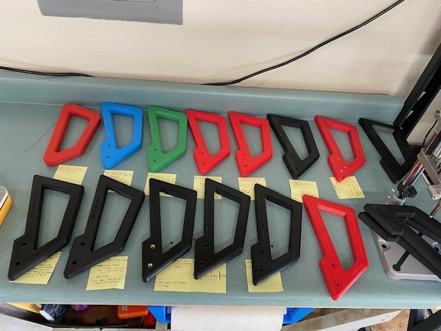 Assorted 3D-printed plastic handles in red, blue, green, and black colors arranged on a table with yellow sticky notes underneath.
