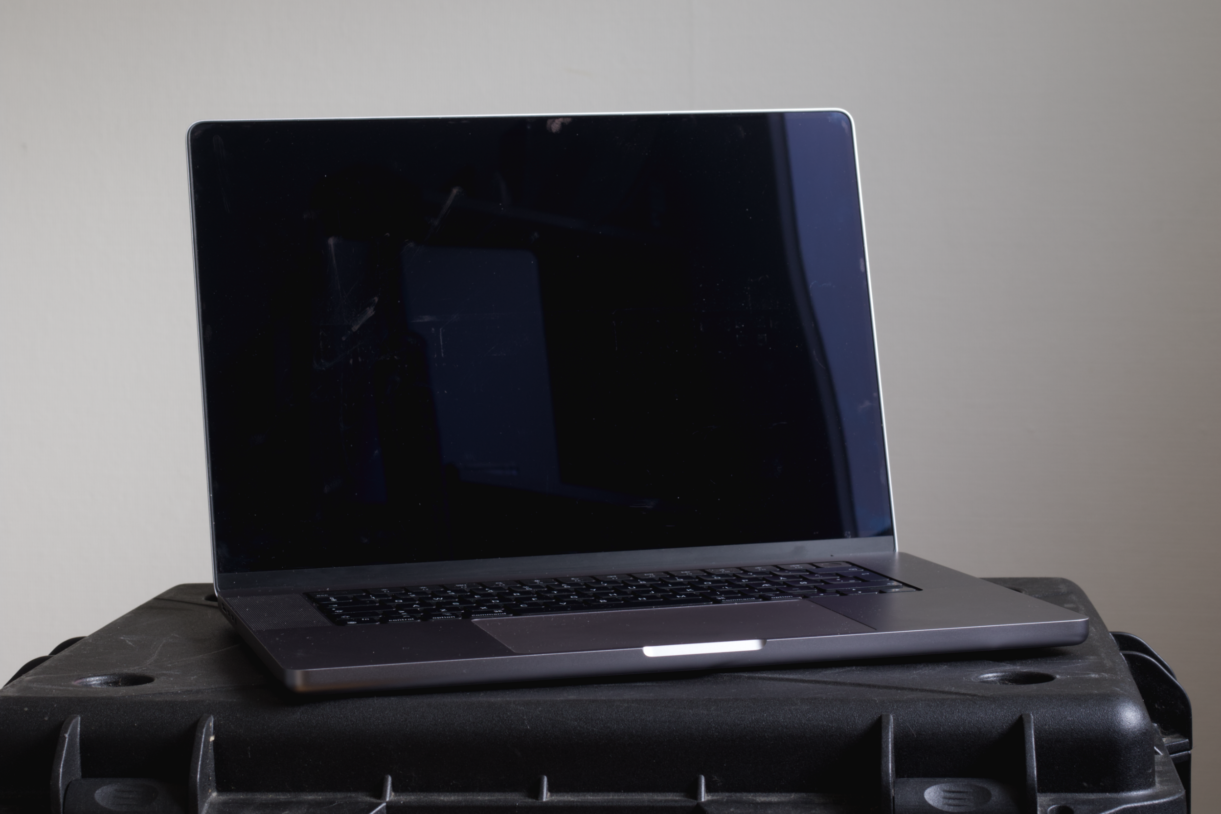 A closed, dark gray laptop with a black keyboard resting on a black plastic case against a plain neutral background.
