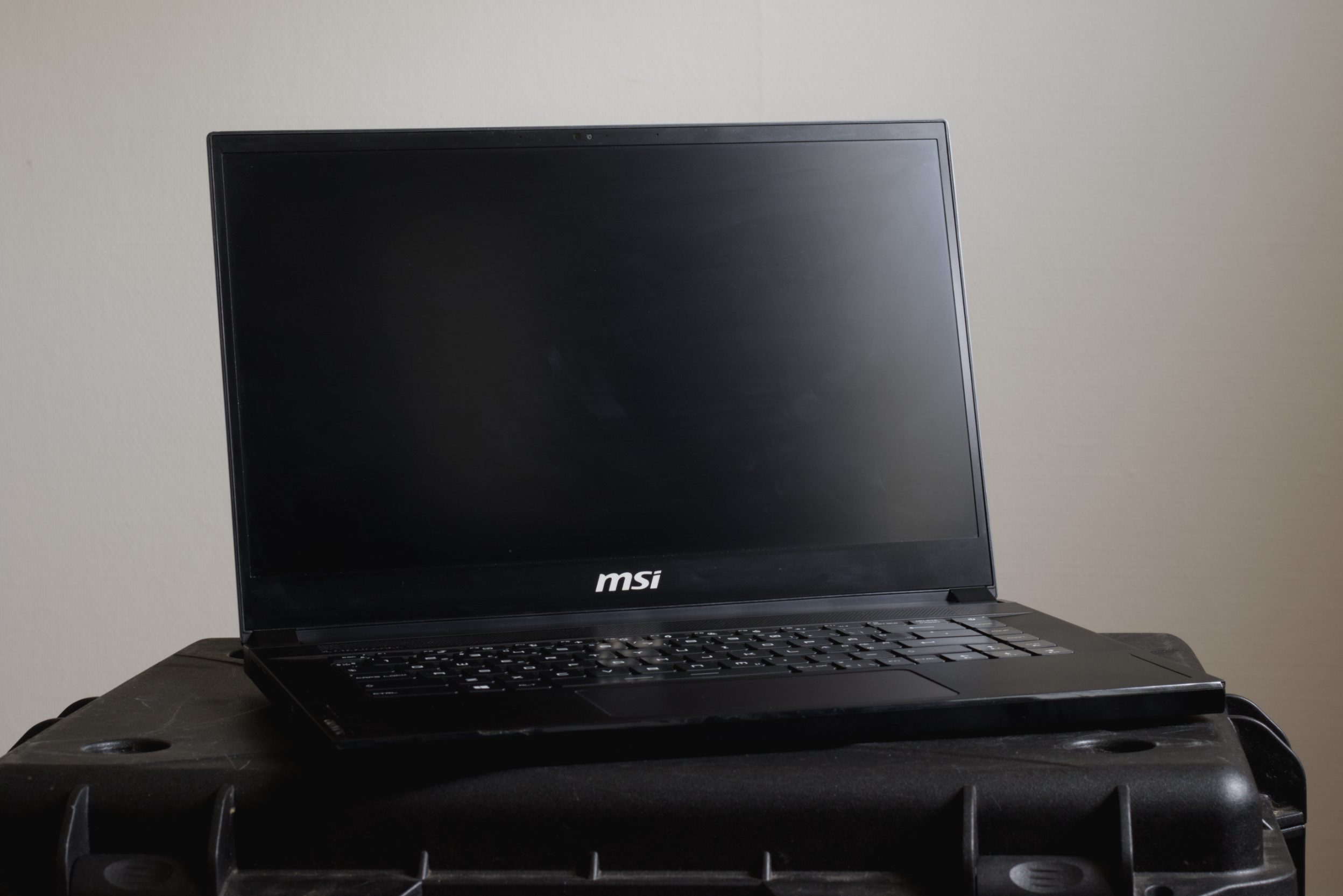 Black MSI laptop placed on a black plastic table with a plain wall background.