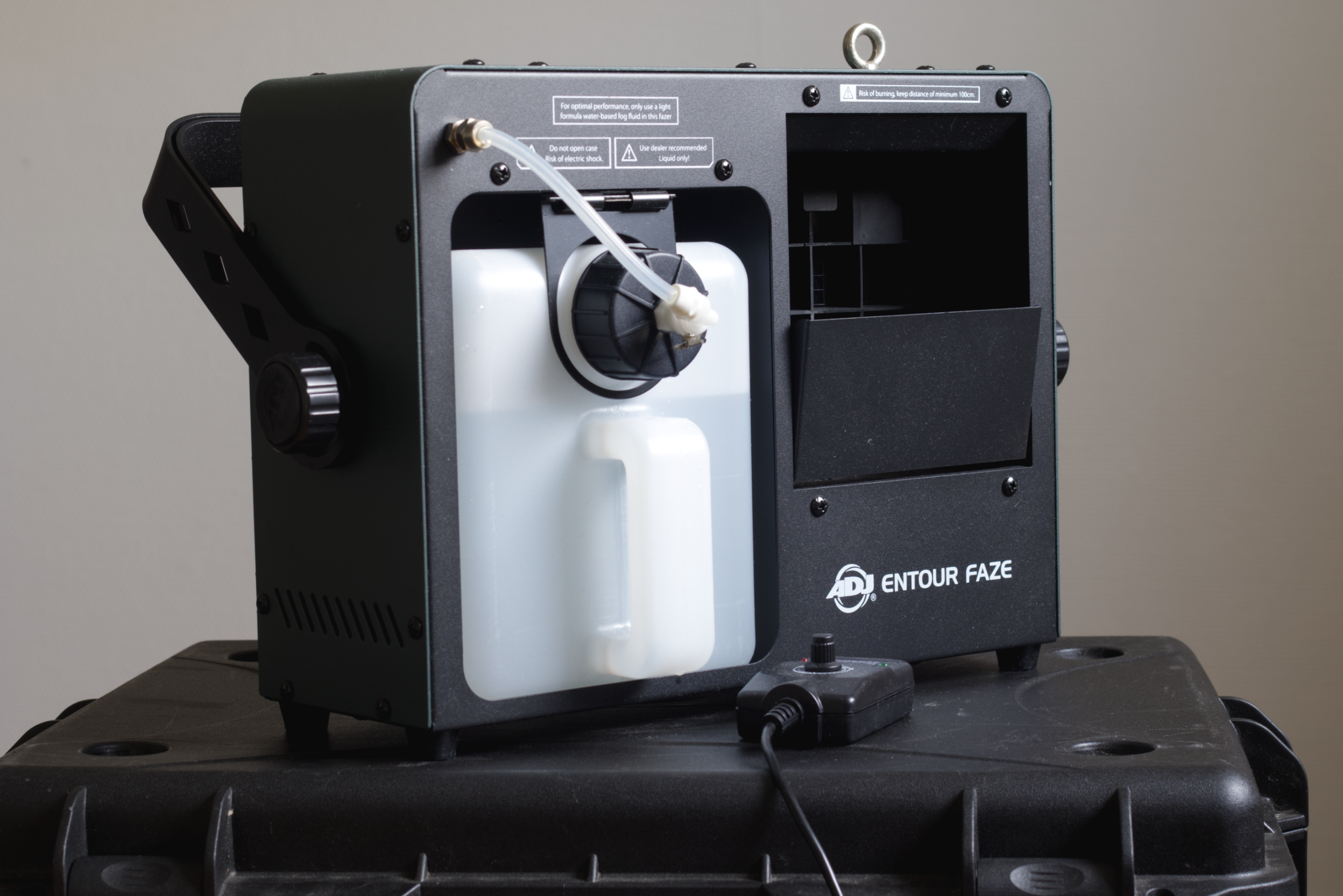 A fog machine labeled 'Entour Faze' with a white fluid tank, tube connected to a black cap, and a remote control on a black case.