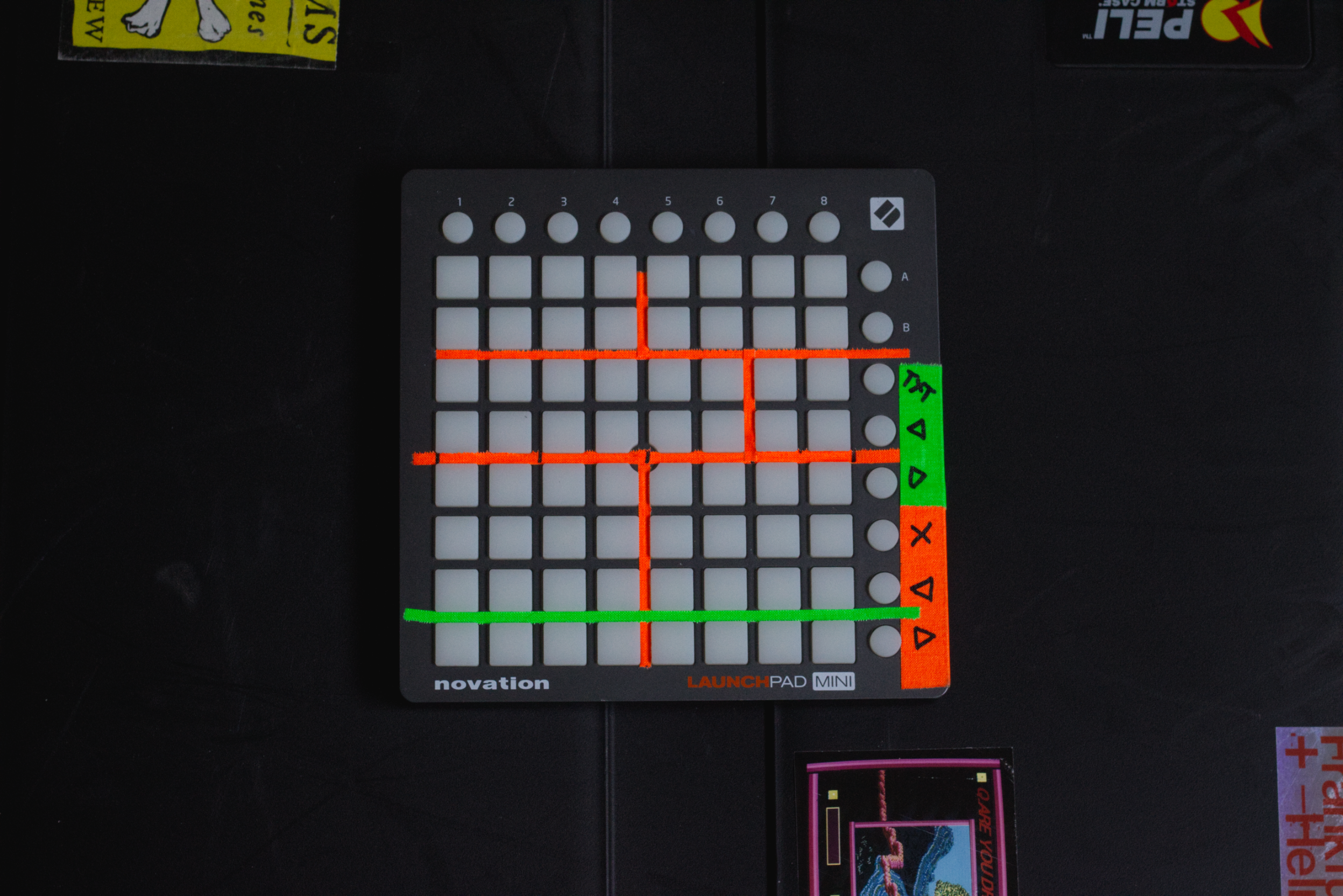 Launchpad Mini grid with red and green markings, located on a black surface with items partially visible around.
