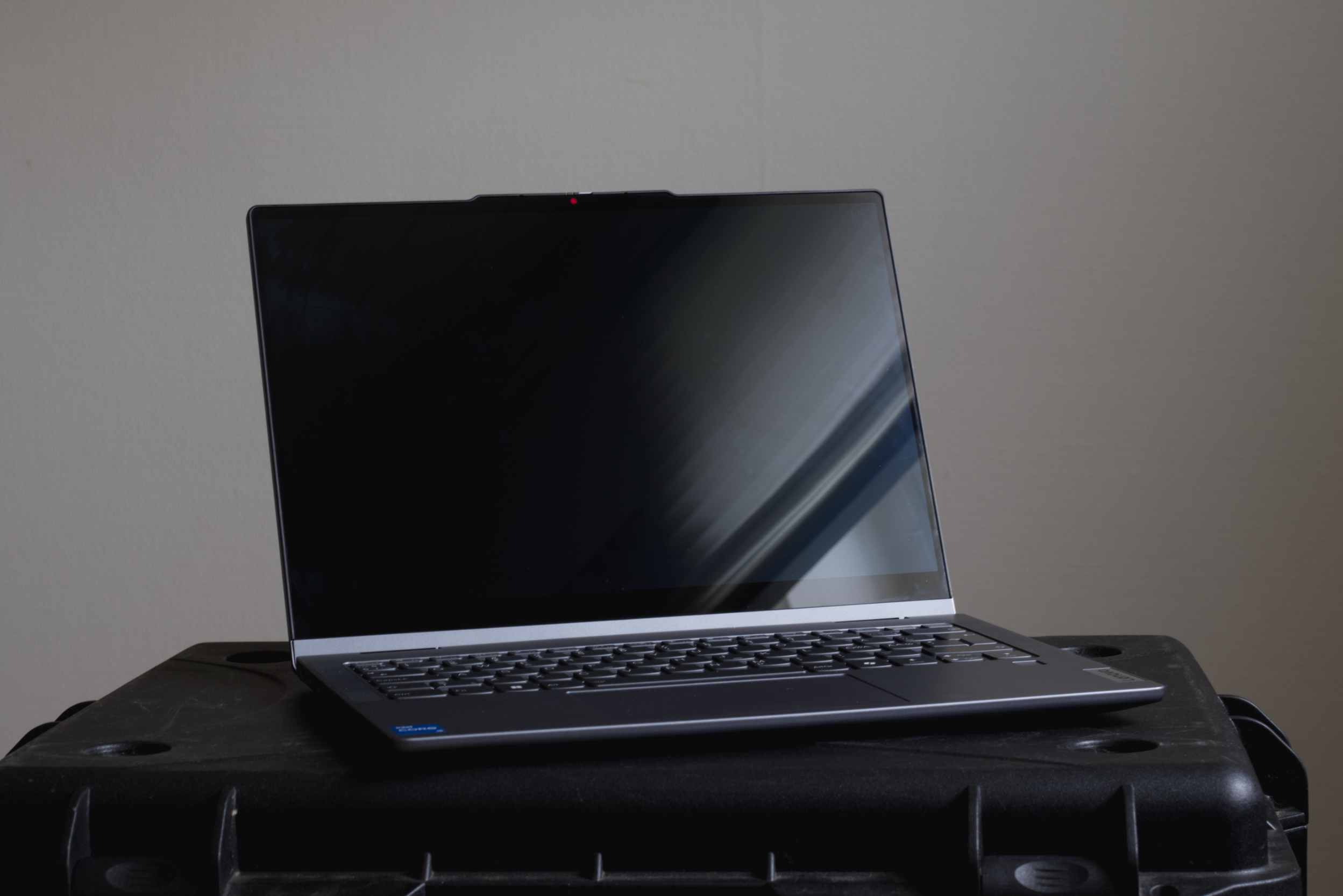 A modern laptop with a dark, reflective screen, placed on a black surface against a plain wall background.
