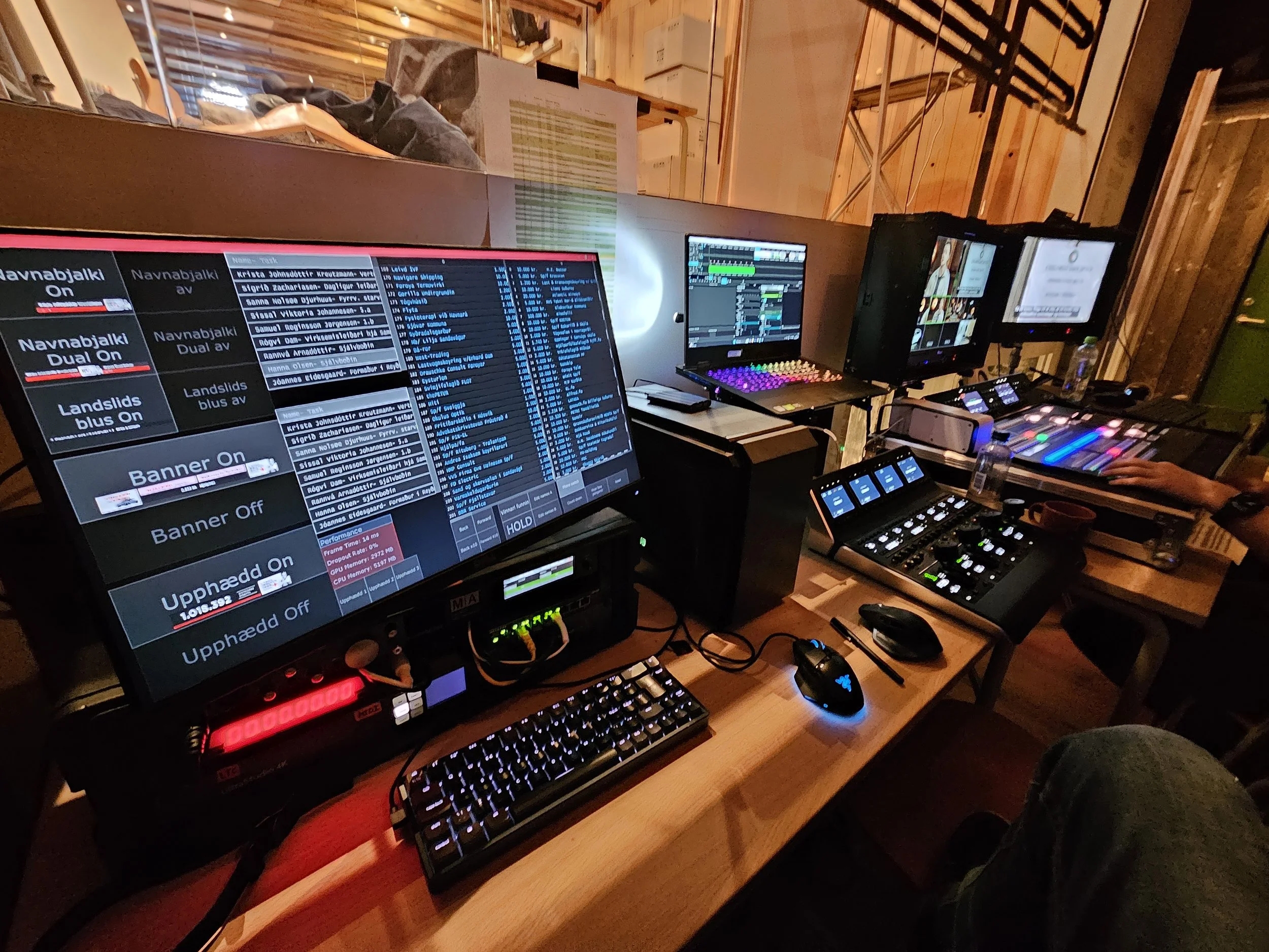 A tech setup with multiple monitors displaying DJ or music production software, a mixer board, a keyboard, a mouse, and various electronic devices in a wooden room.