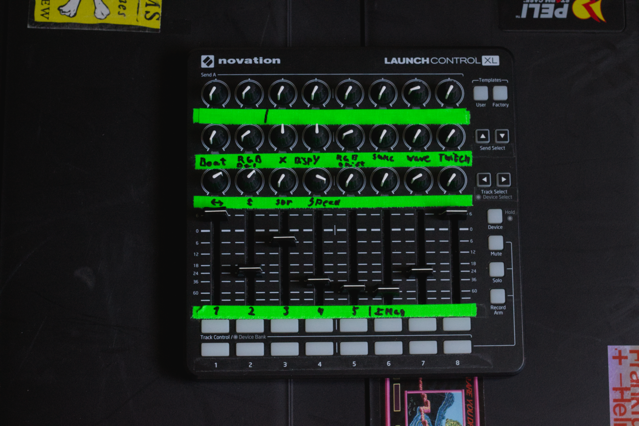 A Novation Launch Control XL MIDI controller with handwritten labels and green tape indicating different functions and settings, placed on a black surface.