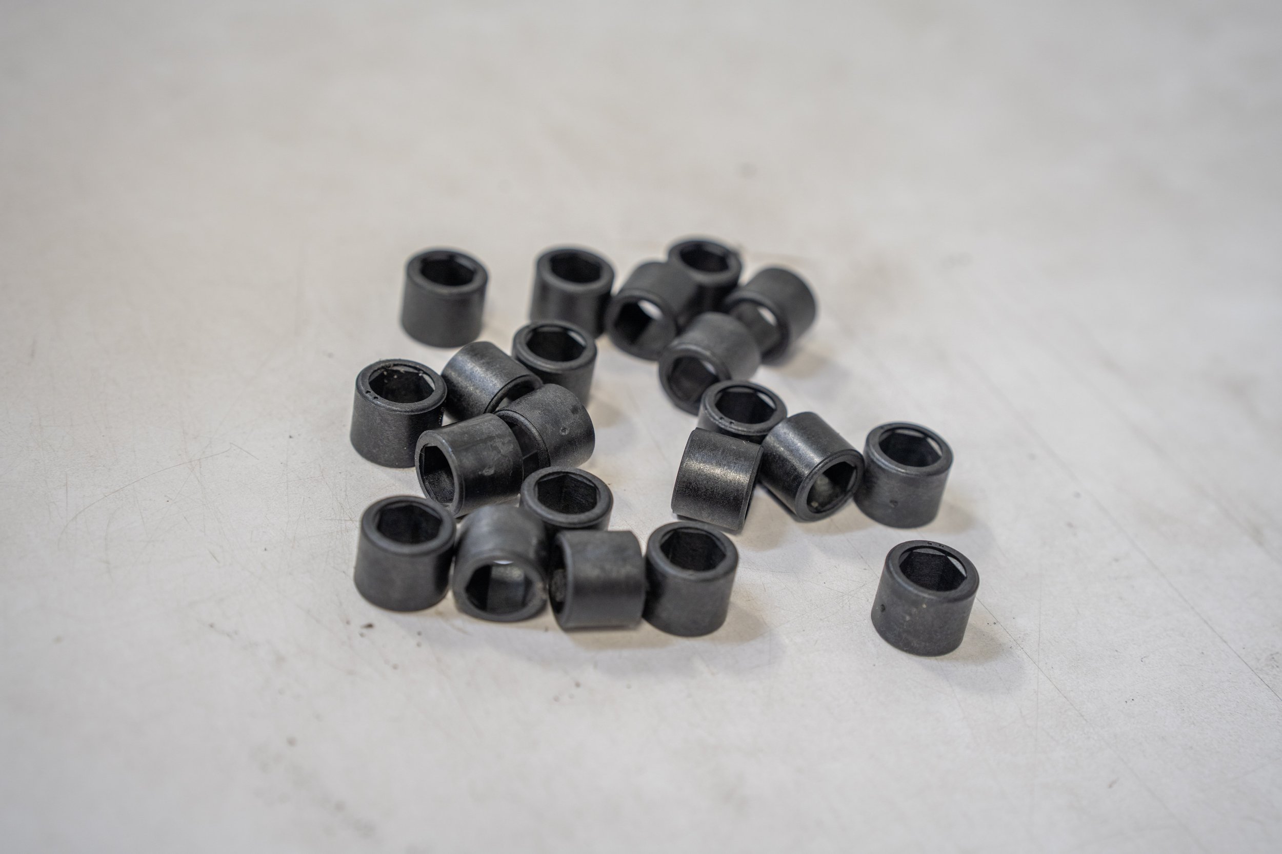 A group of small black rubber grommets scattered on a light-colored surface.