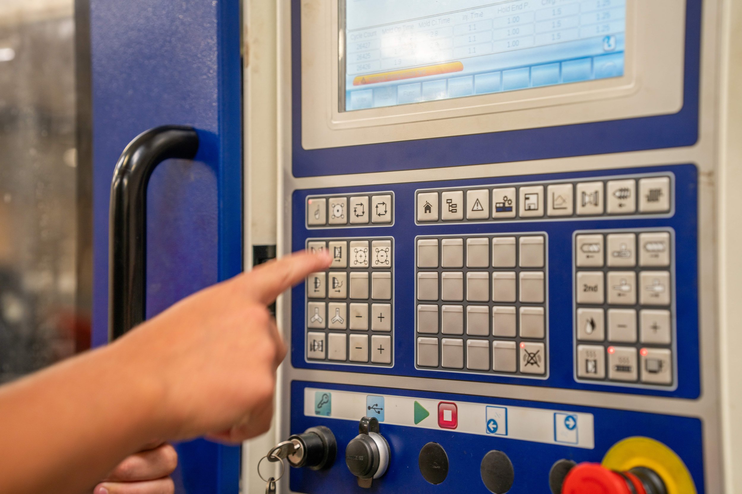 A person's hand pressing buttons on an industrial control panel with a touchscreen and various labeled buttons.