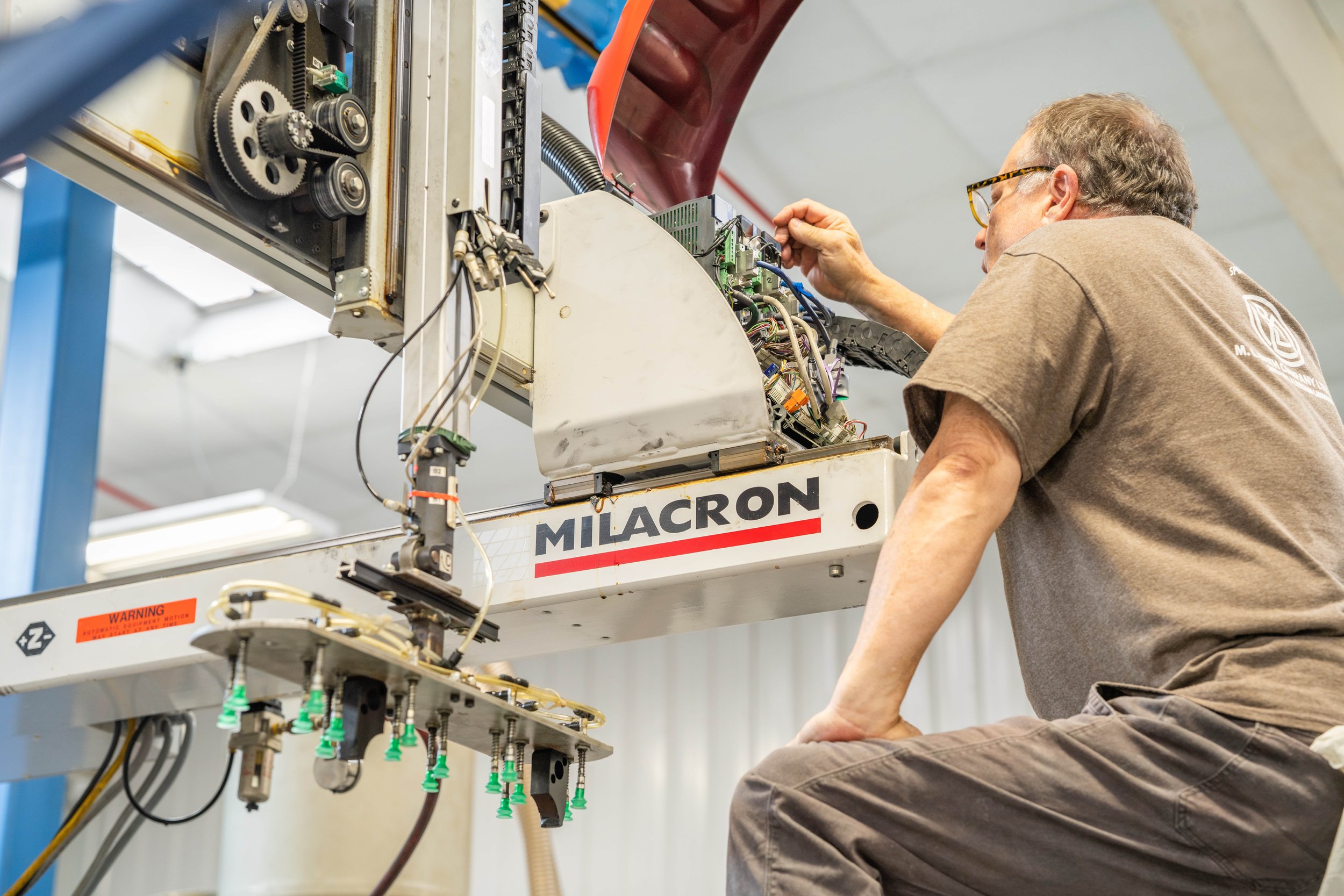 A technician repairs or inspects machinery labeled 'Milacron' in a factory or workshop.