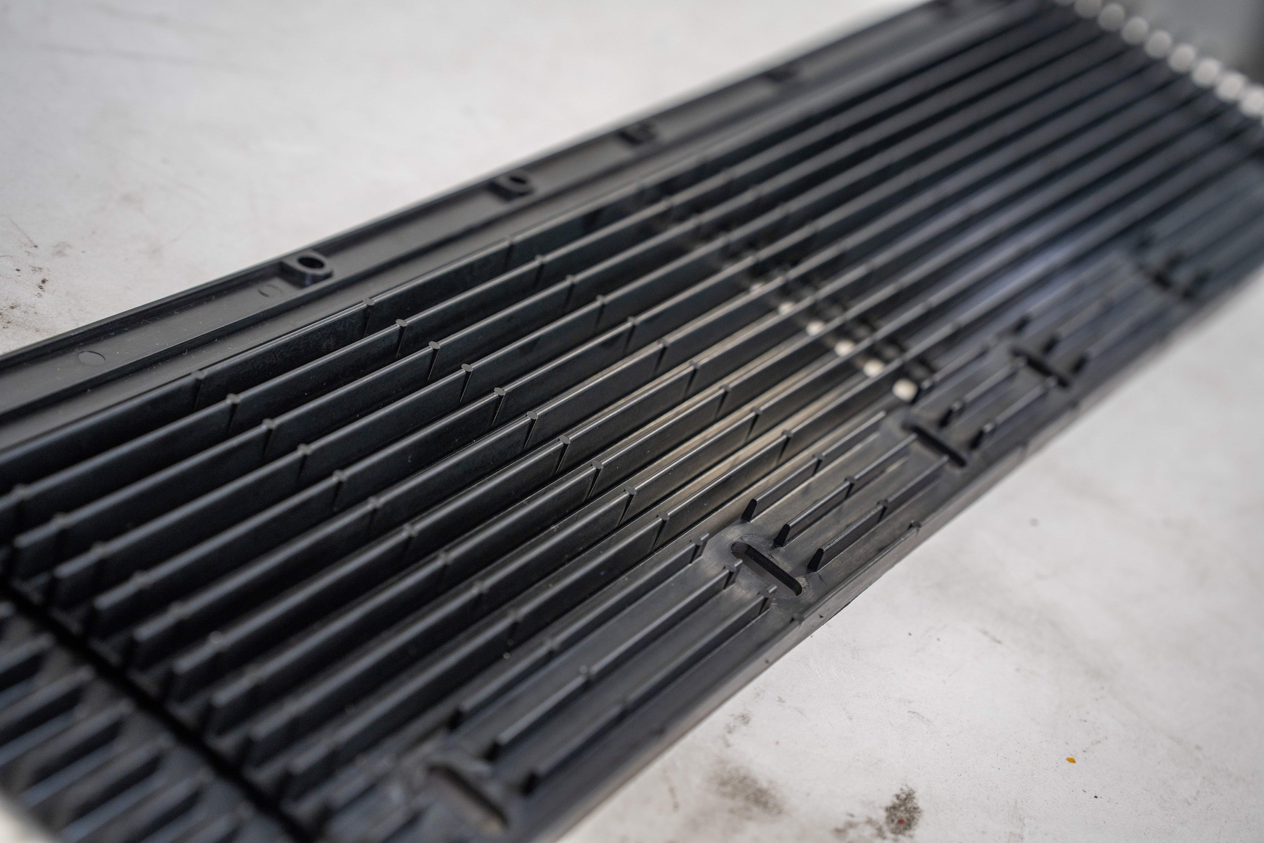A black plastic grating with parallel slats placed on a white surface.
