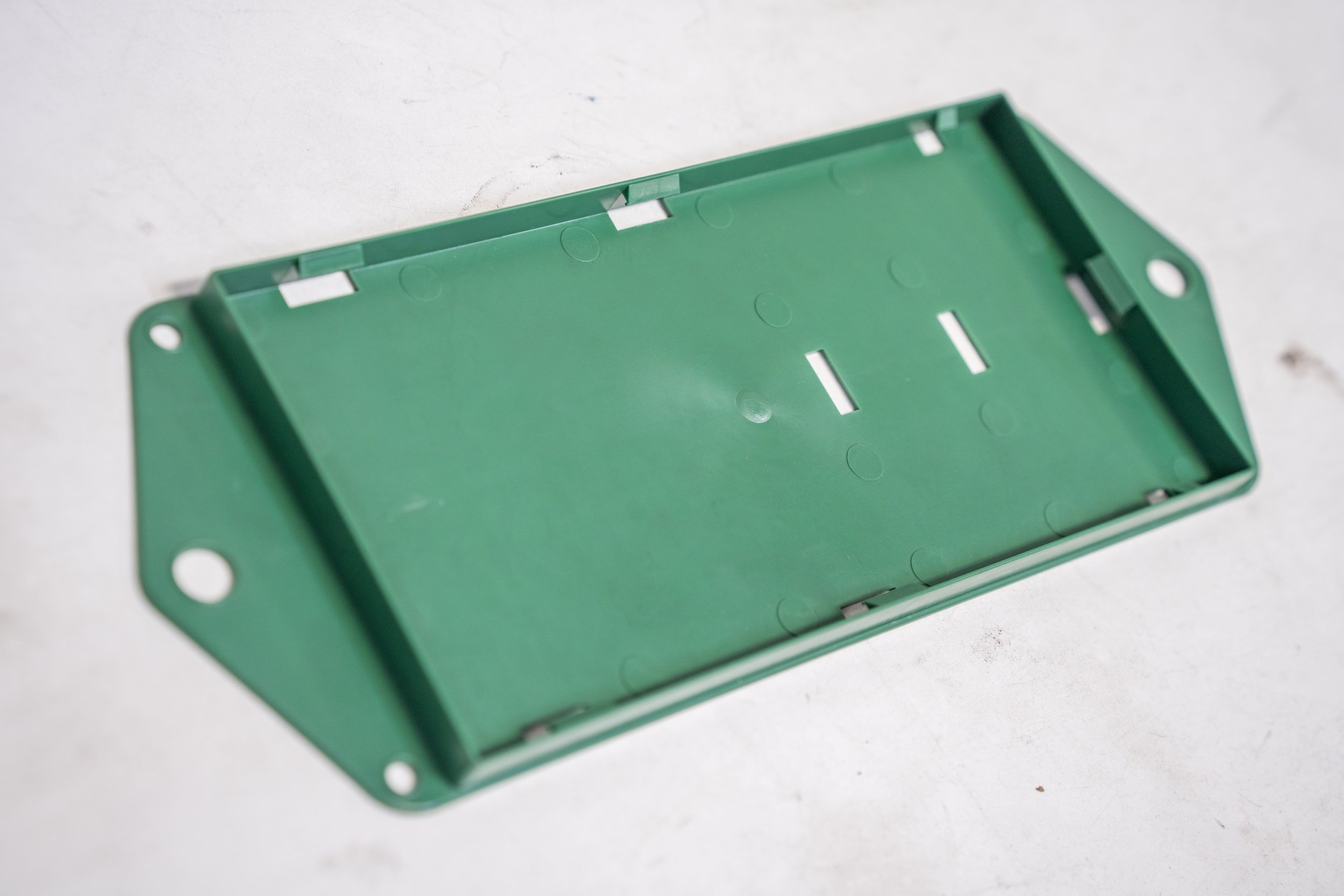Green plastic rectangular electrical junction box with mounting holes on each end, placed on a white surface.