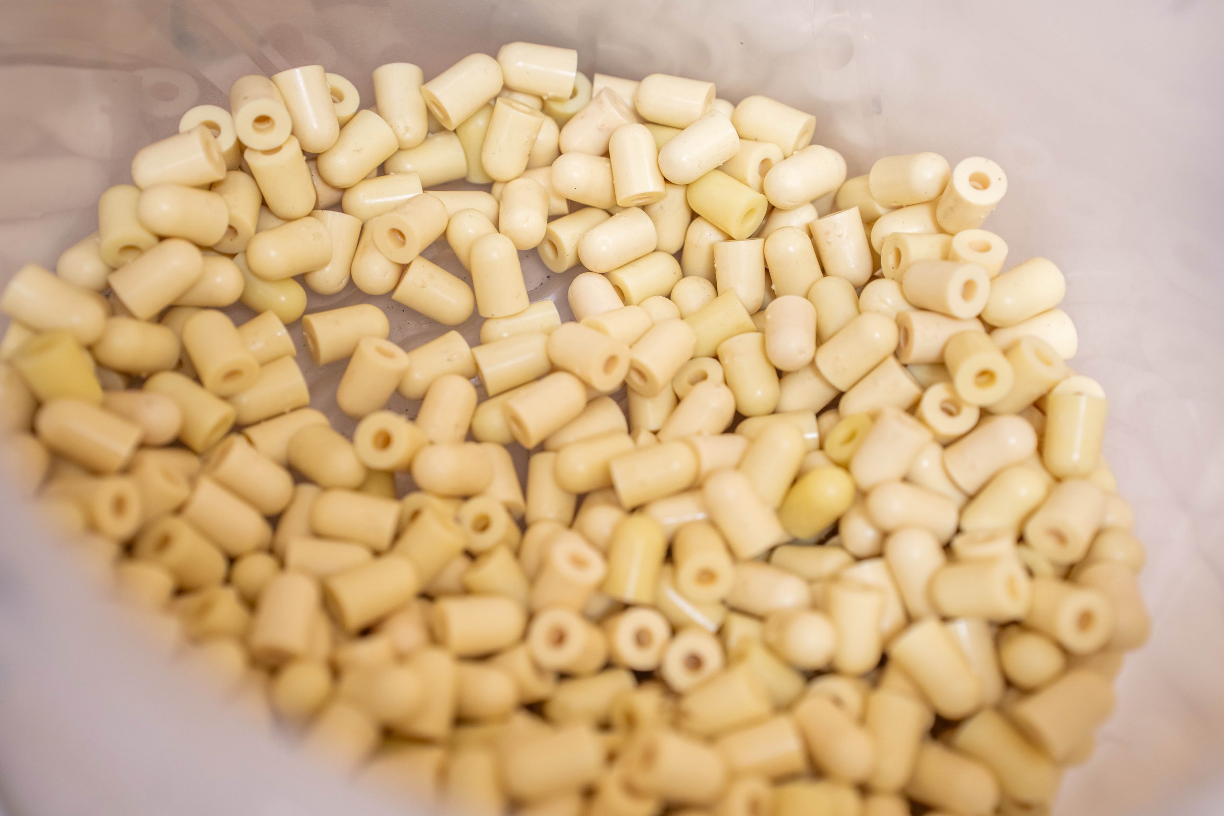 A container filled with small, cream-colored, capsule-shaped food supplements or pills.
