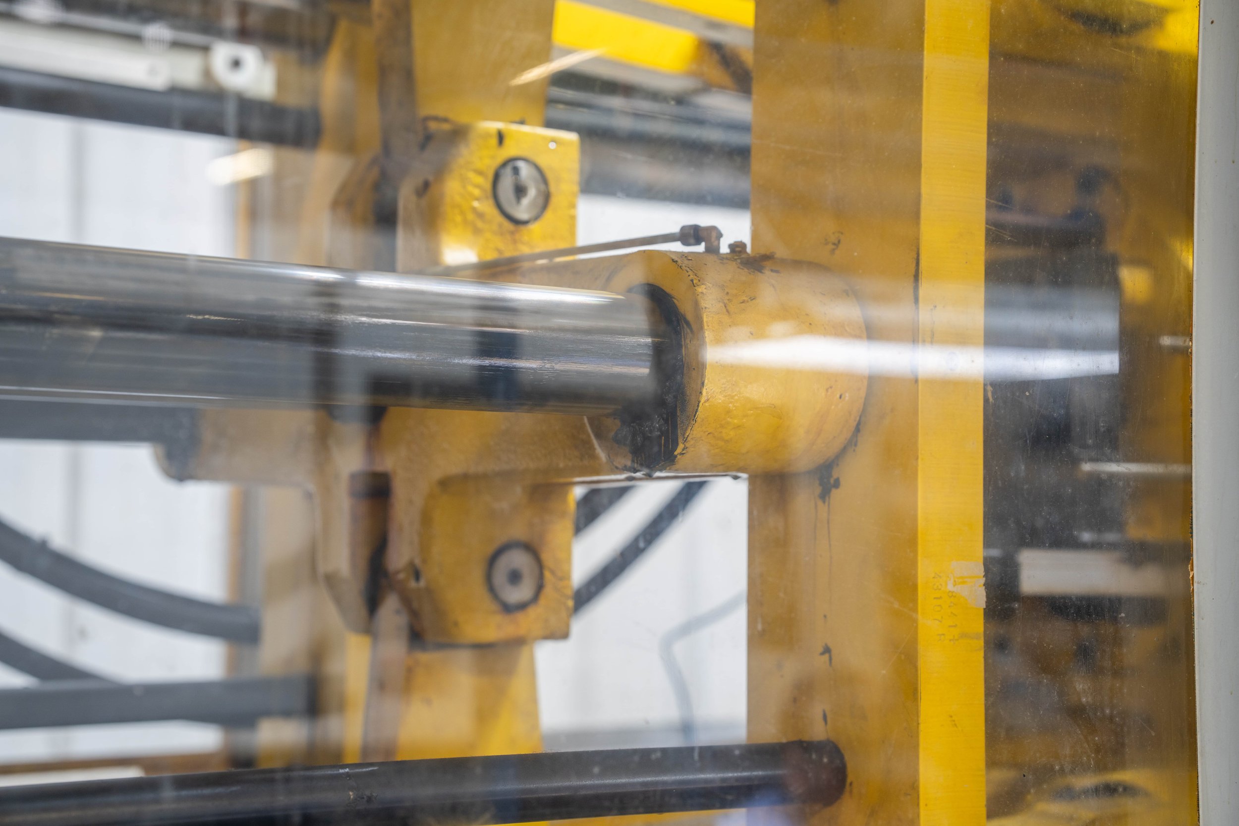 Industrial machine part with a yellow frame and metal rods visible through a glass panel.