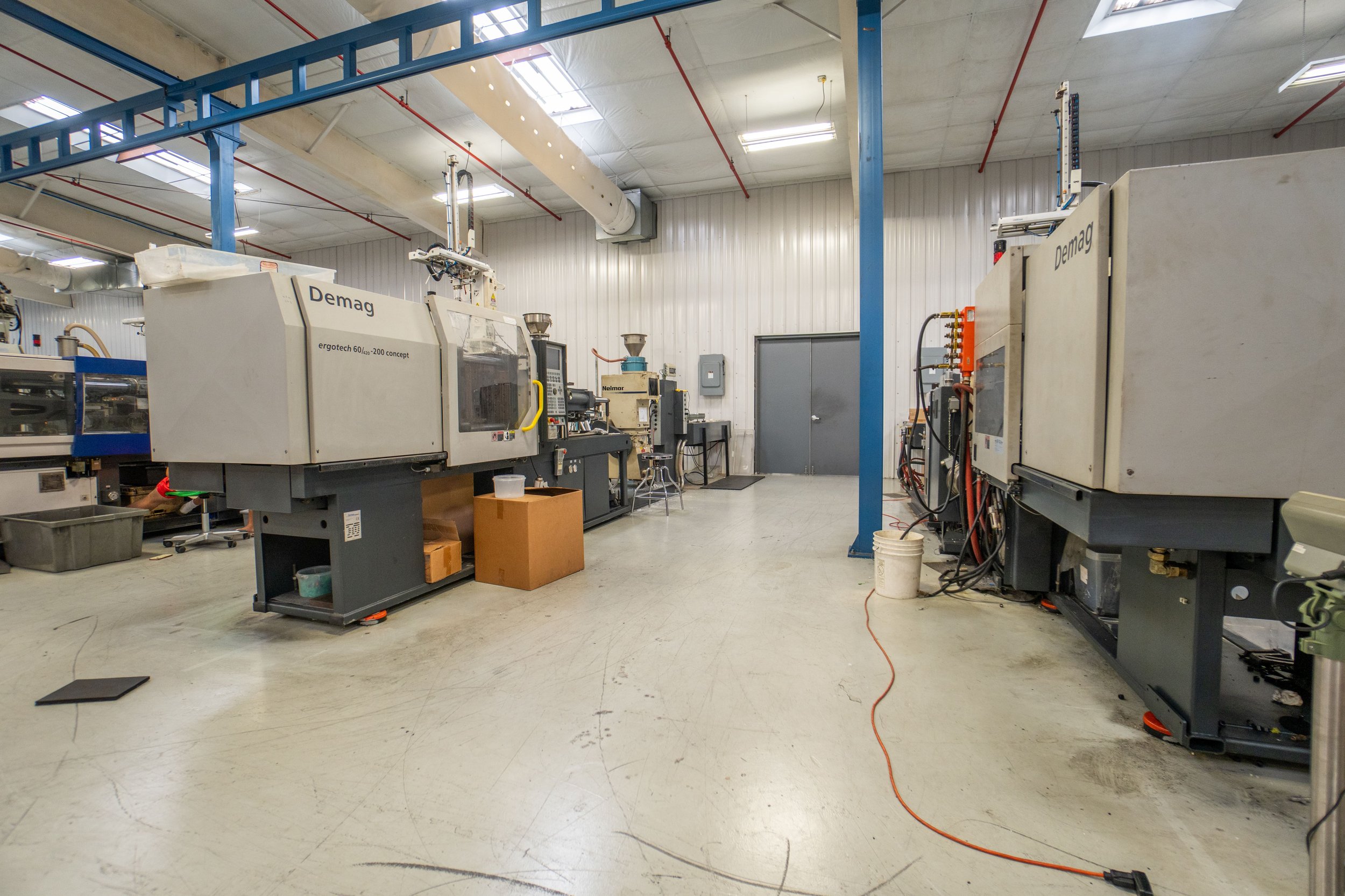 Indoor industrial manufacturing lab with two large Demag machines, workbenches, and equipment, illuminated by ceiling lights and skylights