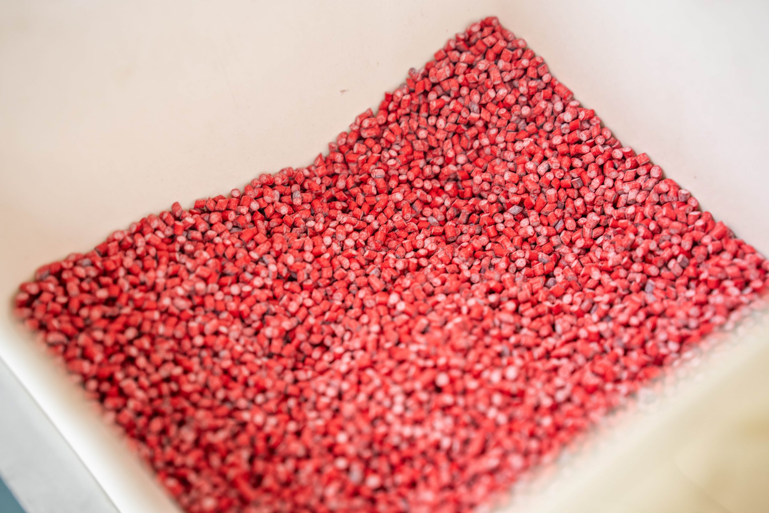Close-up of numerous small, red, pellet-shaped substances in a white container.