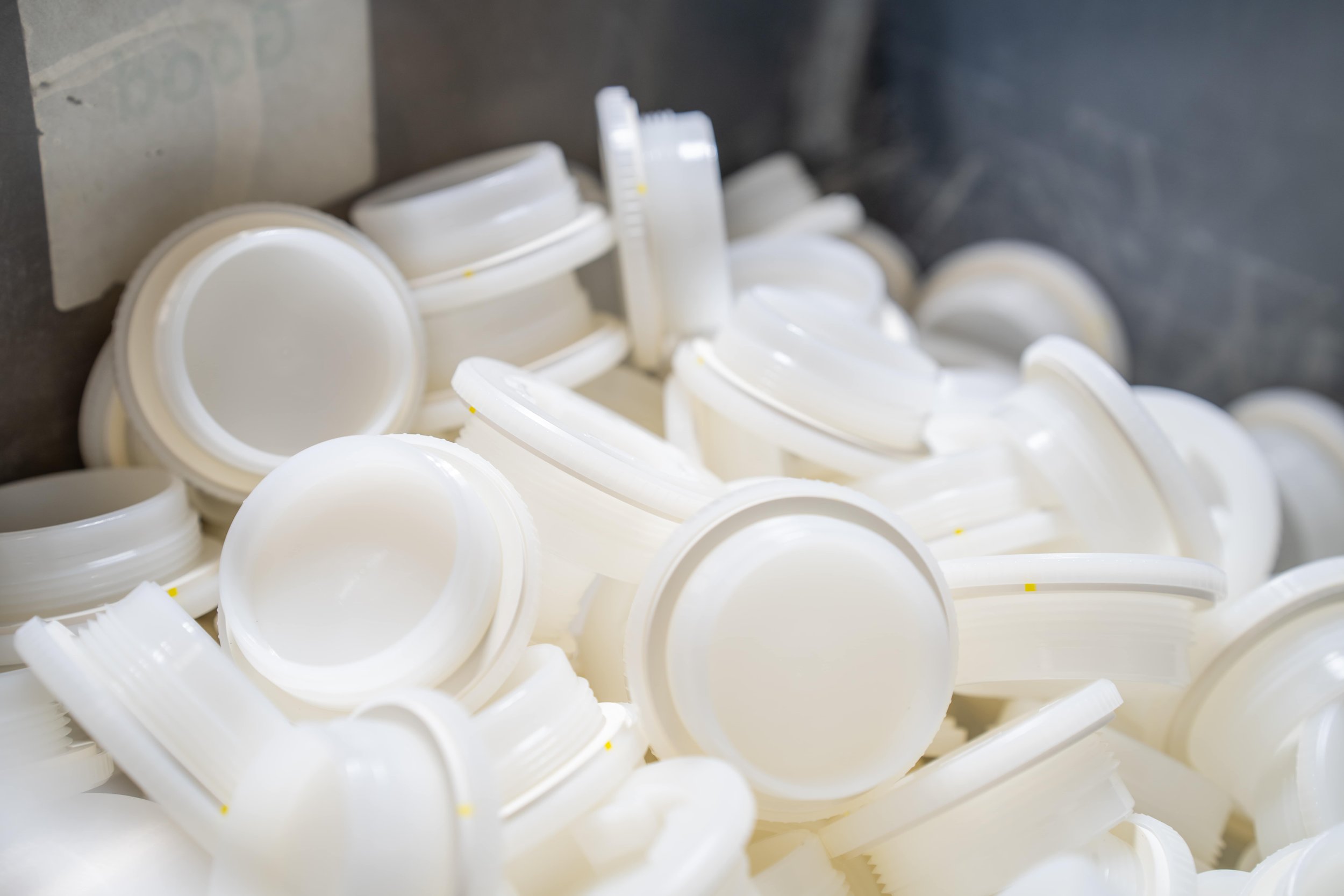Piles of white plastic bottle caps, some upside down, on a dark surface.