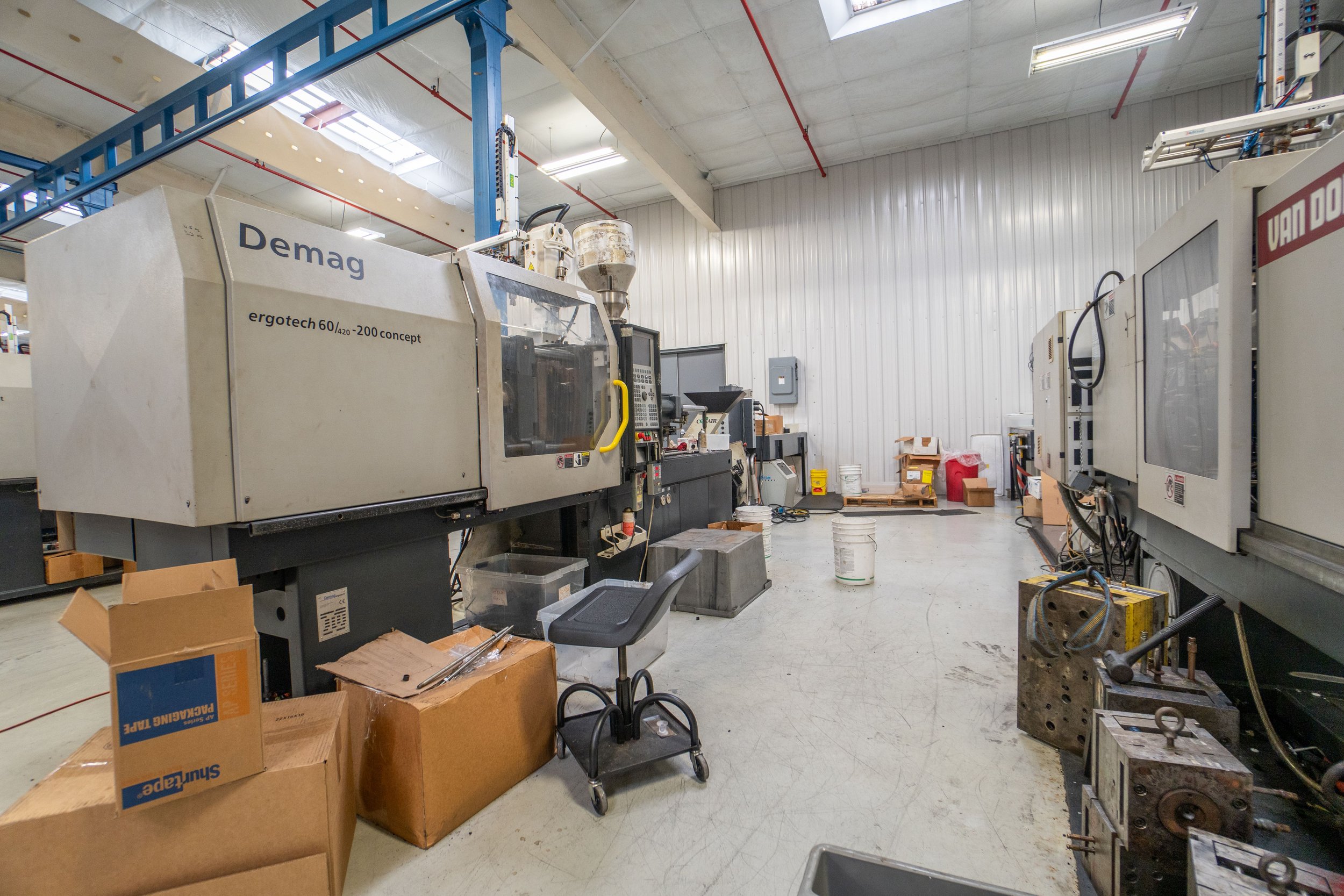 Industrial manufacturing room with CNC machine, cardboard boxes, and various tools and equipment.