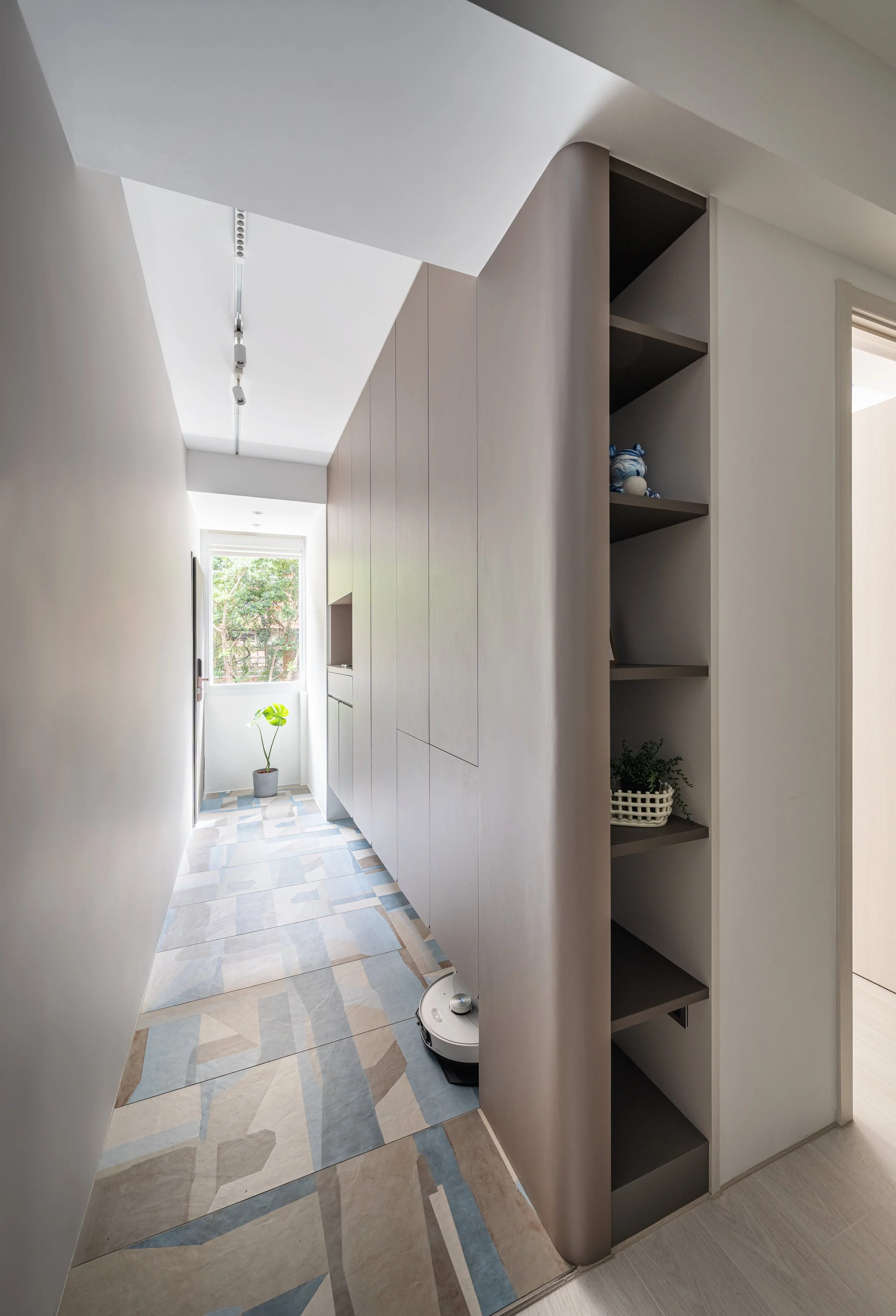 Modern hallway with geometric patterned tiles, a potted plant at the end by a window, and built-in shelving on the right.