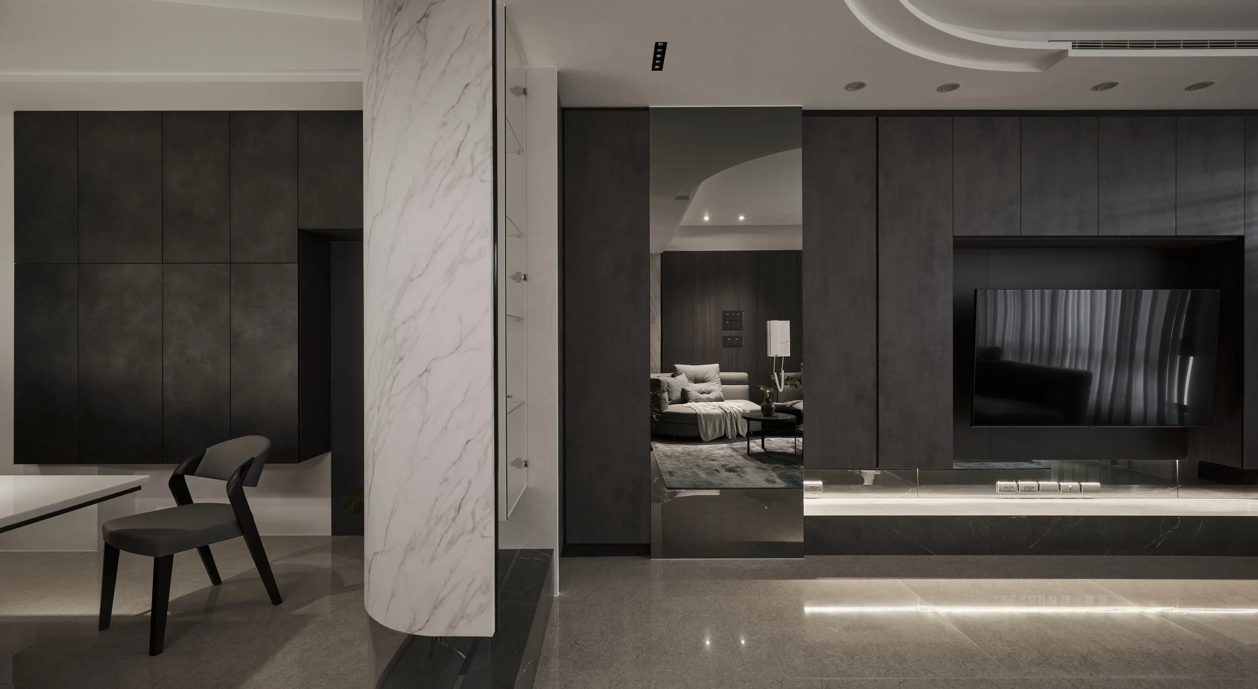 Modern living room with dark wood wall panels, mounted TV, marble accent wall, and gray chairs.
